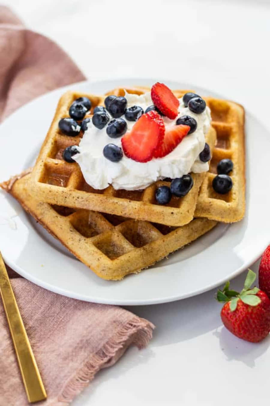 Waffle 桌布 壁紙 — 金黃色窩夫高高疊起，配上忌廉、藍莓和切片草莓，放在白色碟上。