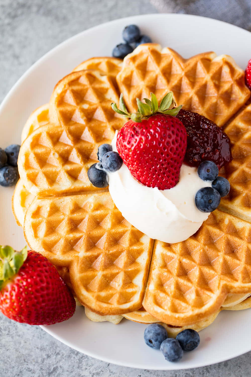 Waffle 桌布 壁紙 — 金黃色窩夫高高疊起，配上新鮮草莓、藍莓和忌廉，放在白色碟上。