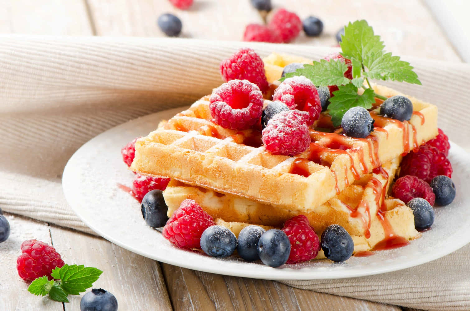 Waffle 桌布 壁紙 — 金黃色窩夫高高疊起，配上新鮮覆盆子、藍莓和薄荷，淋上糖漿，放在質樸的木桌上。