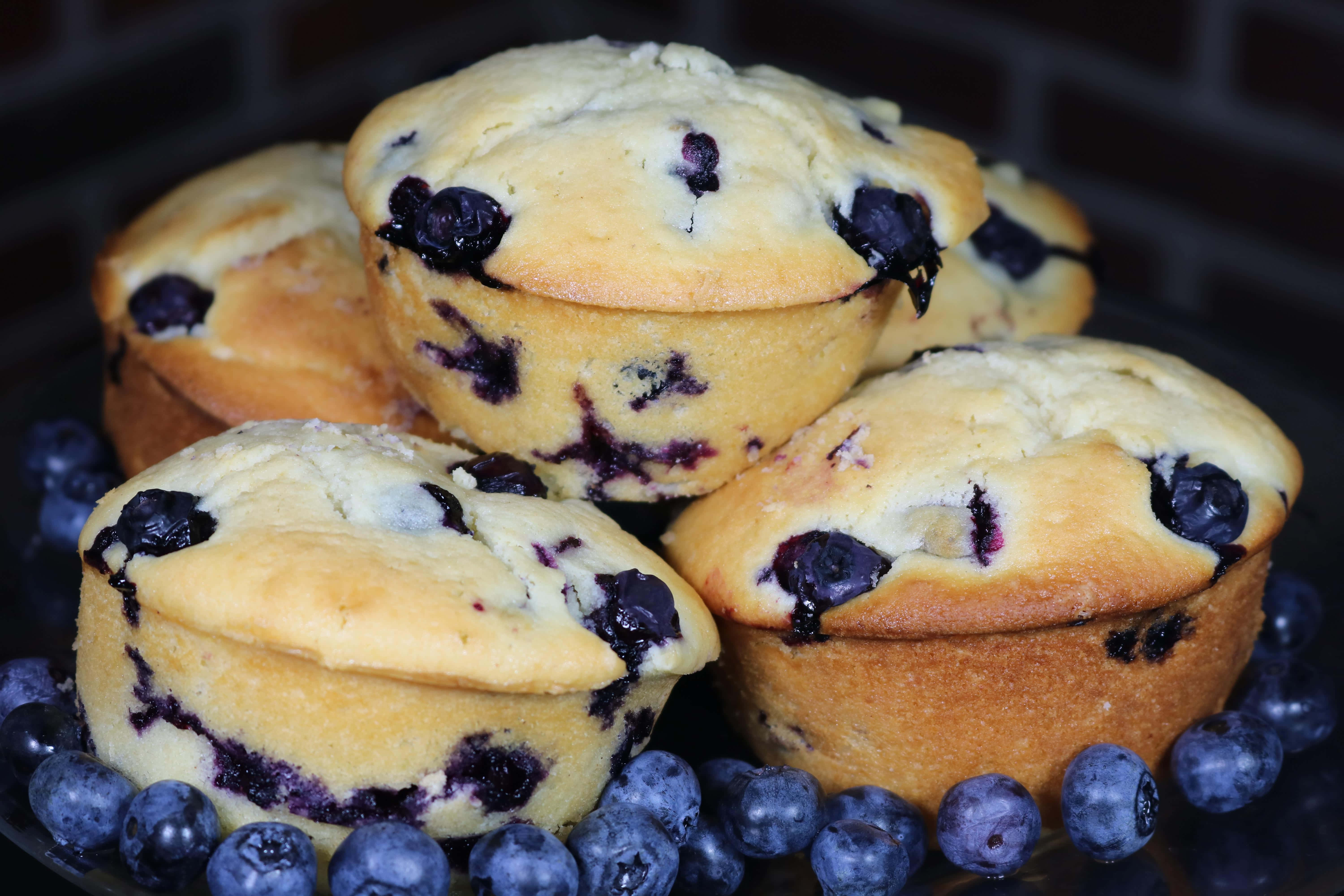 Blueberry Muffins 桌布 壁紙 — 金黃藍莓鬆餅高高堆疊，新鮮莓果在柔和光線下閃閃發光。
