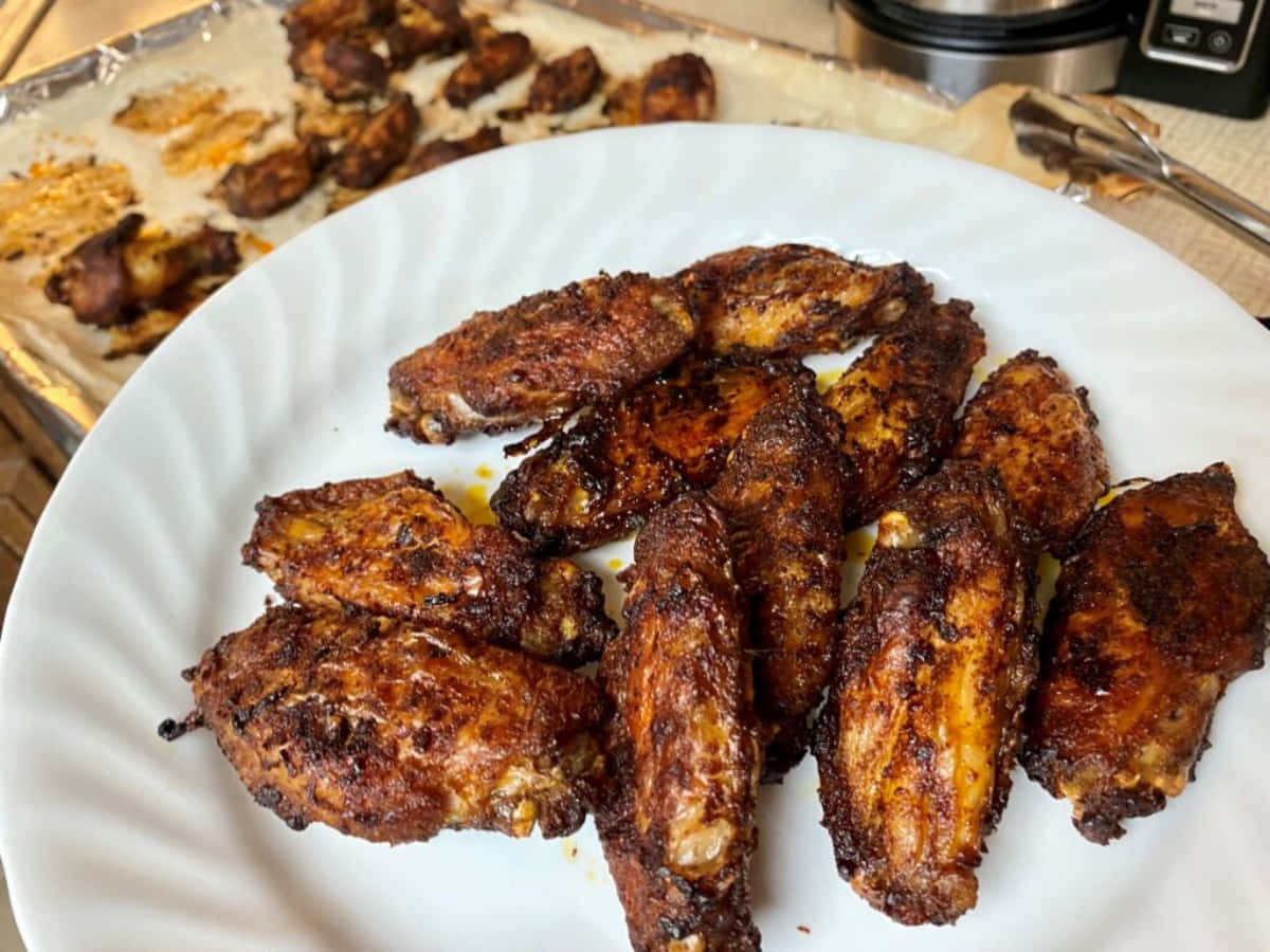Blackened Chicken 桌布 壁紙 — 金黃酥脆的雞翼高高堆在白色碟上，後面有更多雞翼放在鋪了錫紙的烤盤上。