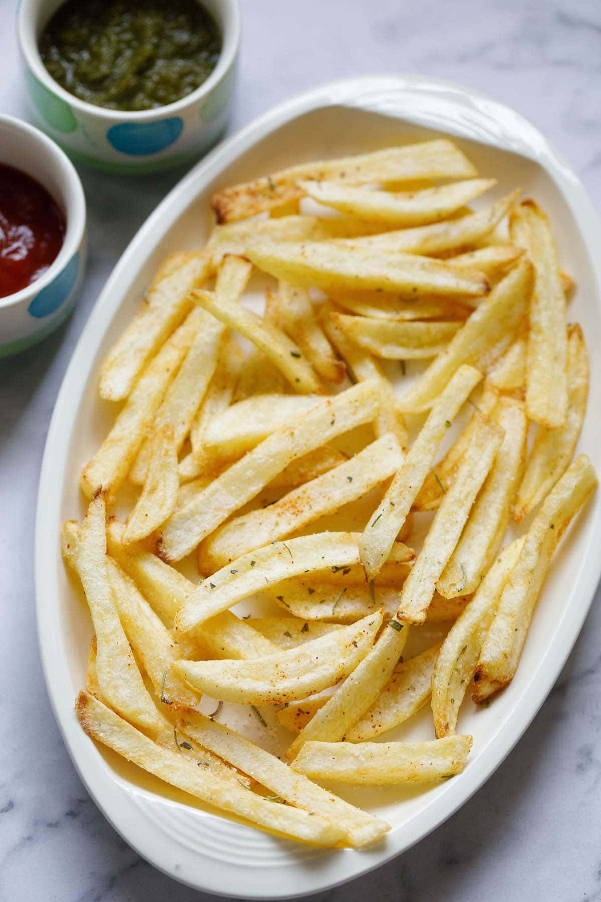 French Fries 桌布 壁紙 — 金黃酥脆的香草調味薯條，盛載於白色碟上，配以圖案碗中的茄汁和綠色醬汁。