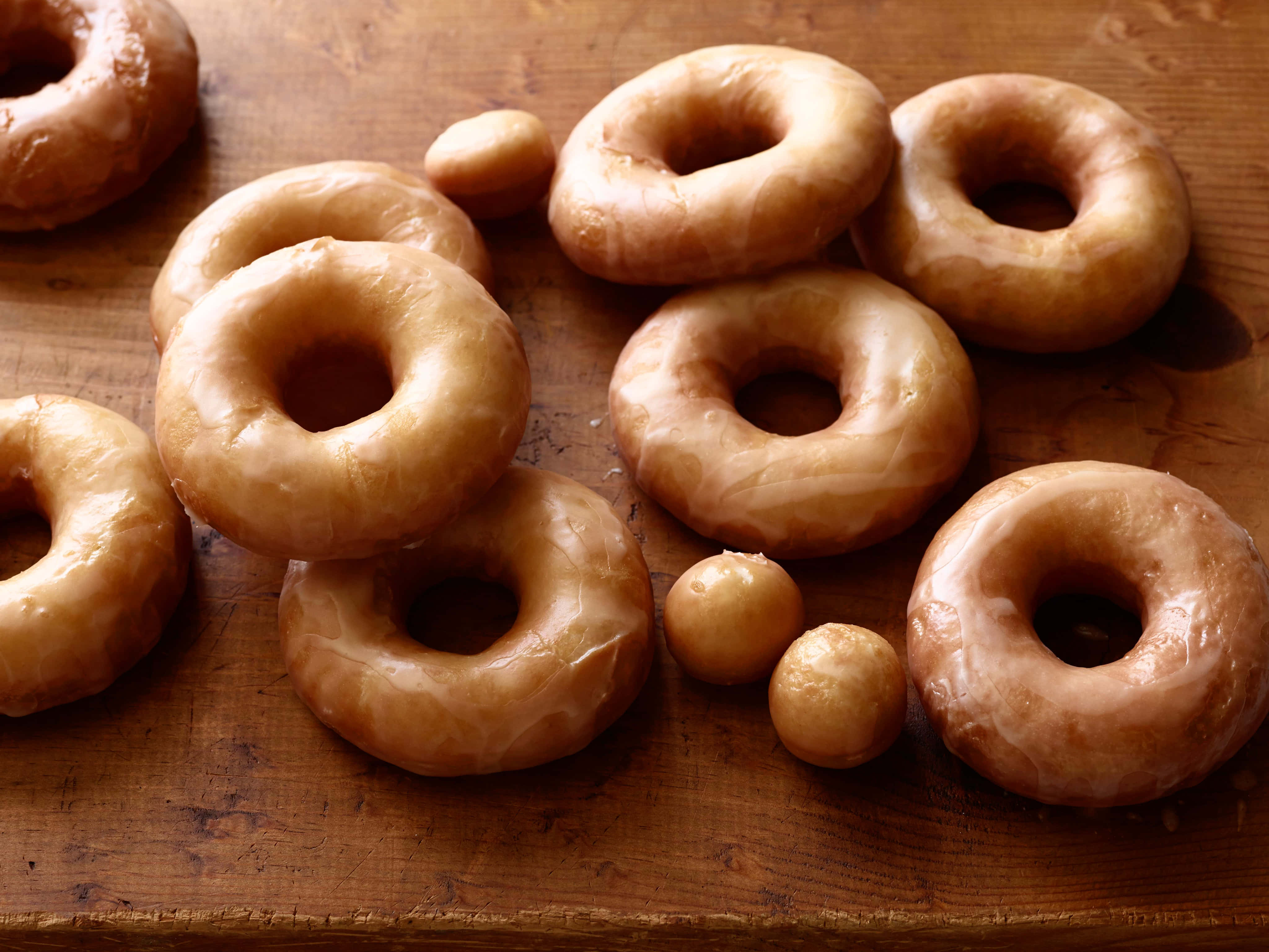 Glazed Donut 桌布 壁紙 — 金黃釉面冬甩和迷你冬甩在溫暖自然光下，誘人地放在質樸的木質表面上。