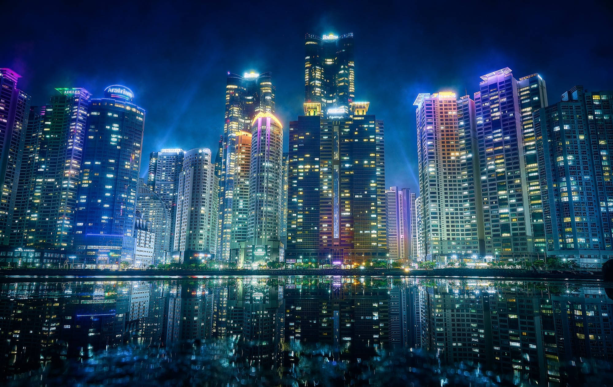 釜山大都會城市 壁紙 — 令人驚嘆的夜景，高聳的摩天大樓與鮮豔的霓虹燈完美倒映在平靜的水面上。