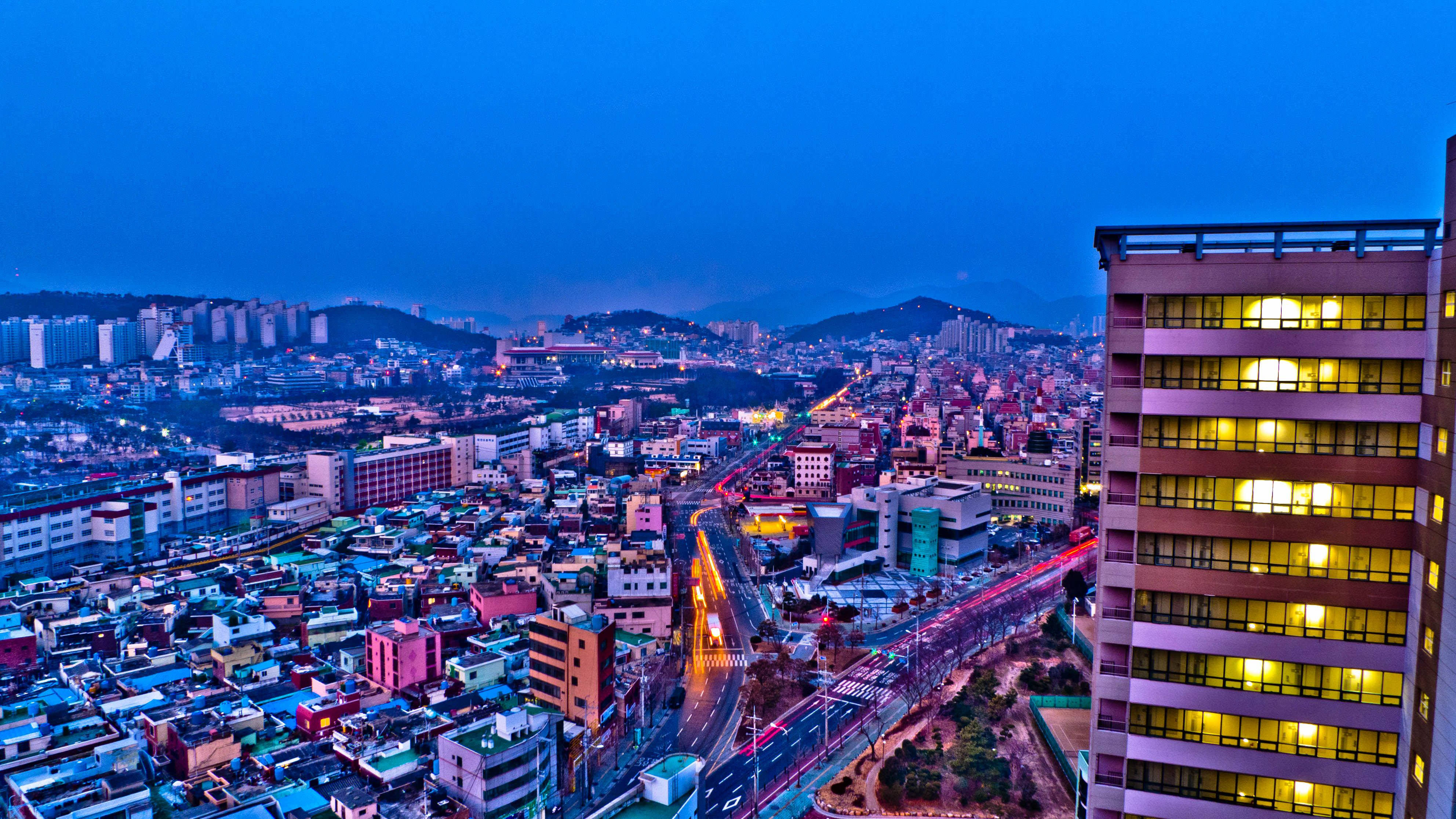 釜山都市風景 壁紙 — 在深藍色天空的襯托下，一個充滿活力的城市景觀，閃爍的窗戶和流動的交通燈光。