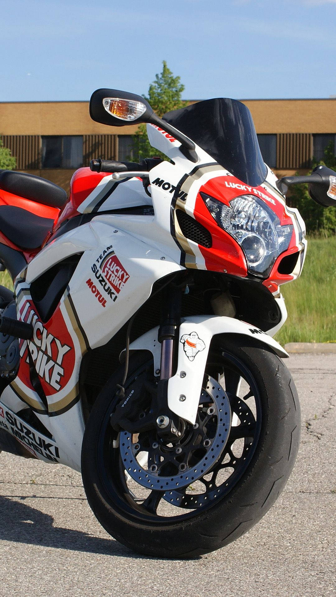 紅白色Suzuki電單車帶有Lucky Strike貼紙，停泊在人行道上。