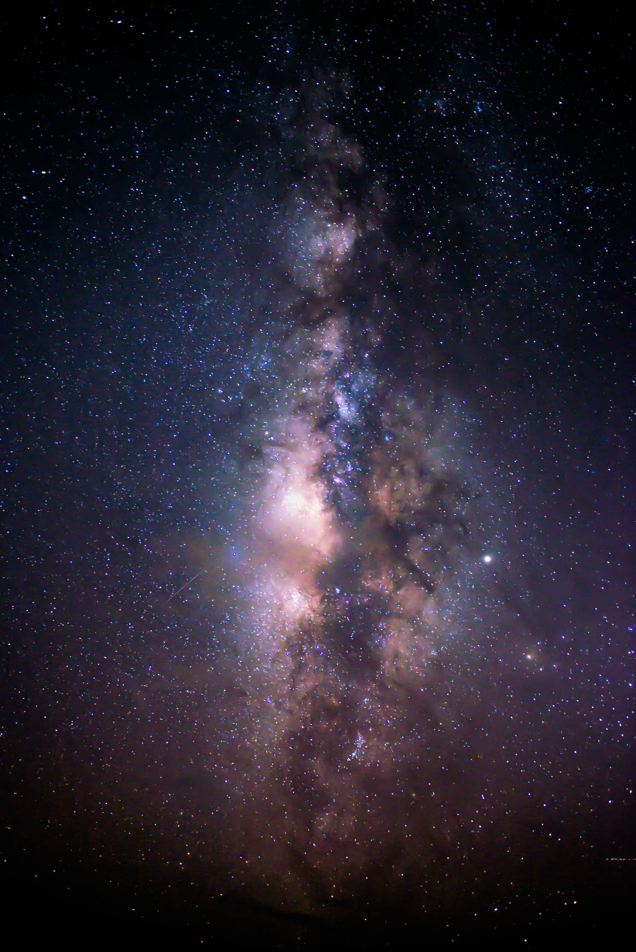 銀河系在繁星點點的夜空中散發出粉紅色和藍色的星雲光芒。