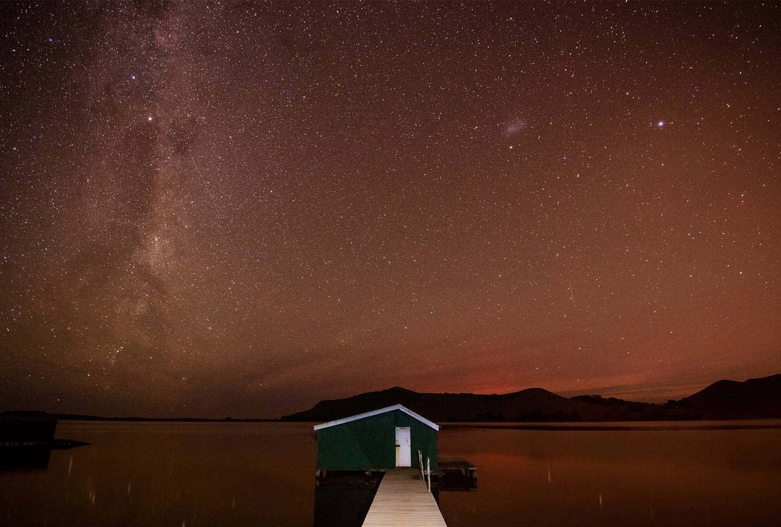 銀河下碼頭上的綠色船屋星空夜景