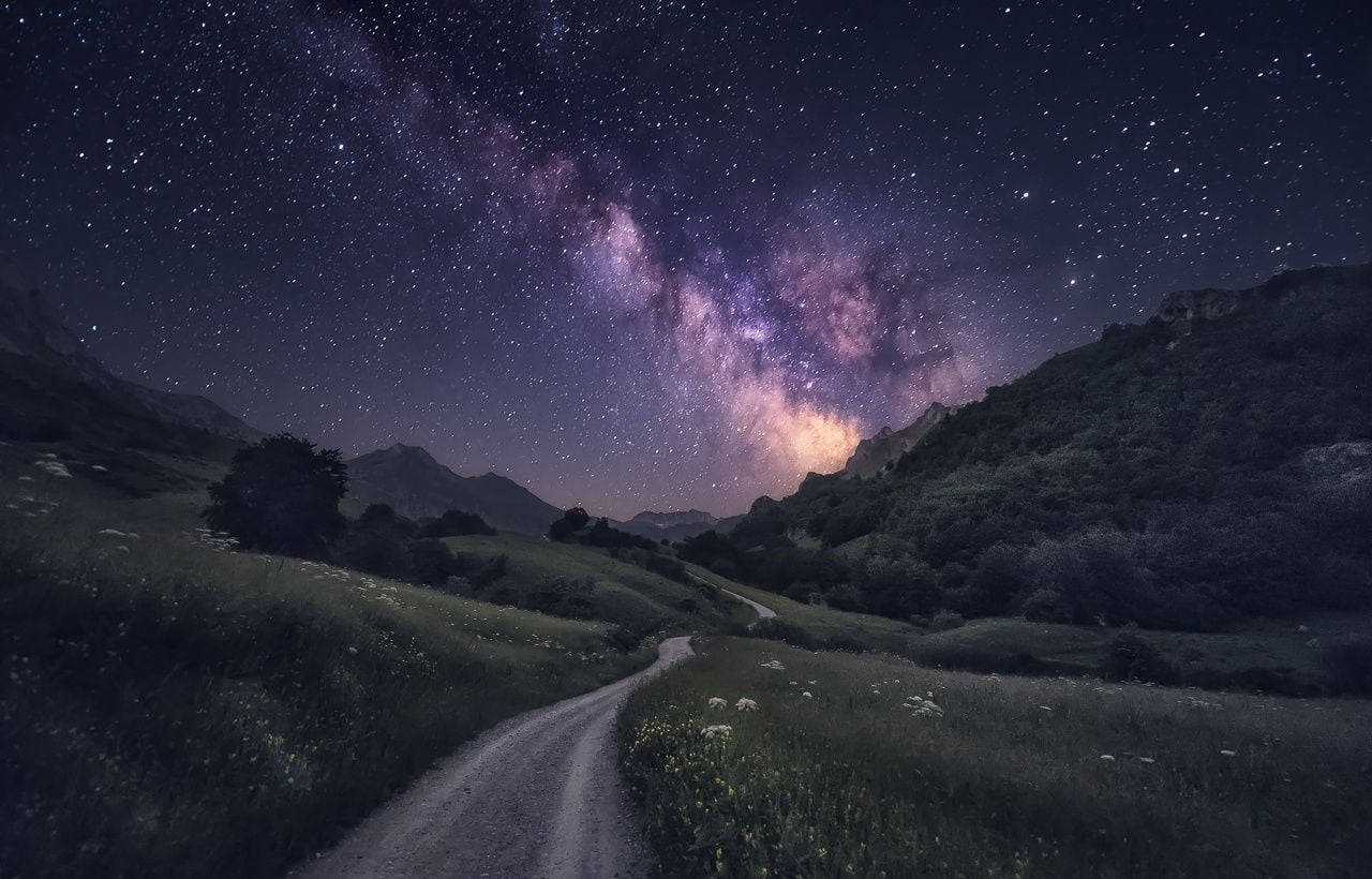 星空之夜，銀河高懸於山巒景觀之上，一條泥土小徑蜿蜒穿過草地。