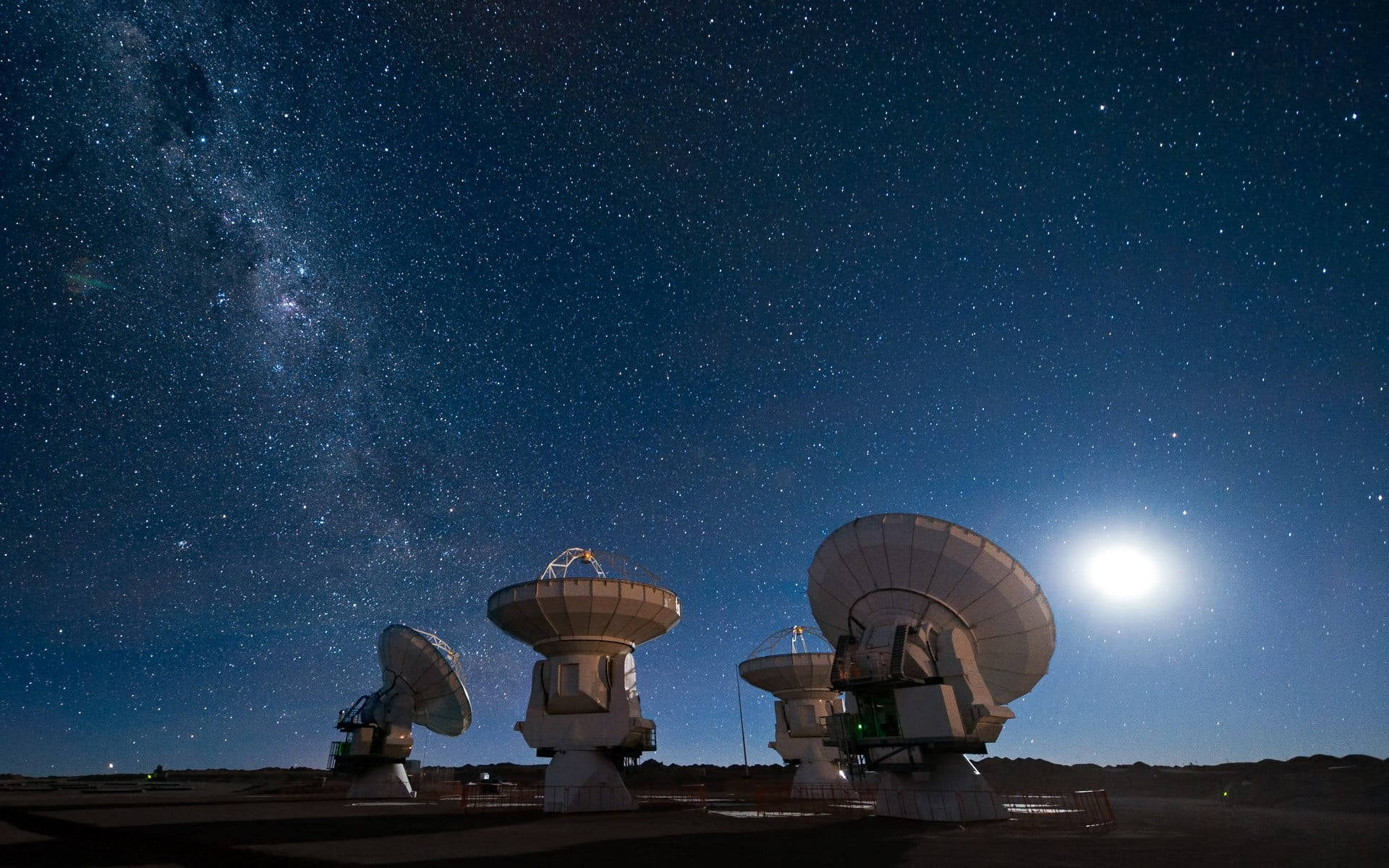 繁星點點的夜空下，可見銀河和月亮的無線電望遠鏡。