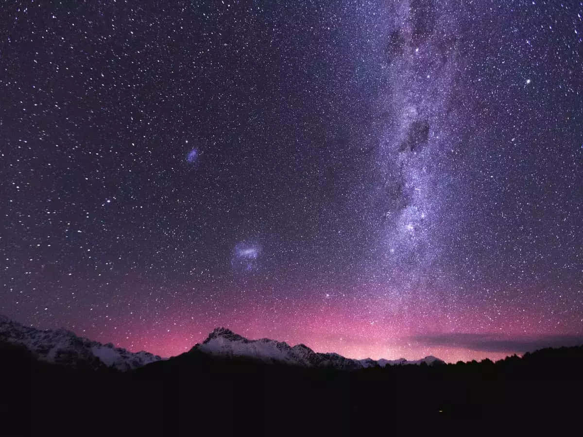 銀河與繁星高懸於山巒之上 壁紙 — 令人嘆為觀止的夜空佈滿繁星，銀河在充滿活力的粉紅色極光下拱起在積雪的山峰之上。