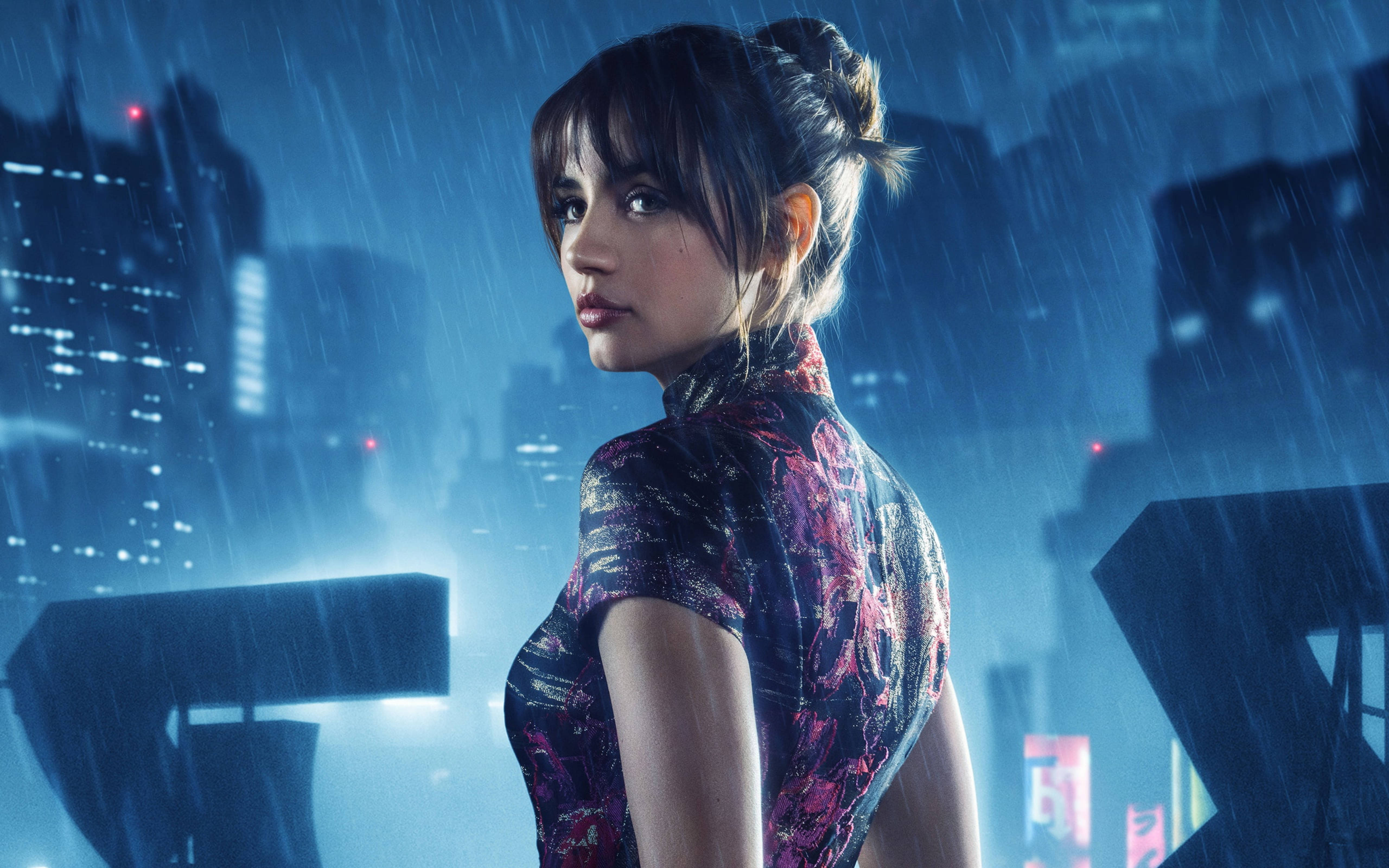 銀翼殺手2049 安娜·德·阿瑪斯雨中 壁紙 — 一位身穿圖案連衣裙的女性在雨中站立，背景是夜晚霓虹燈閃爍的未來城市景觀。
