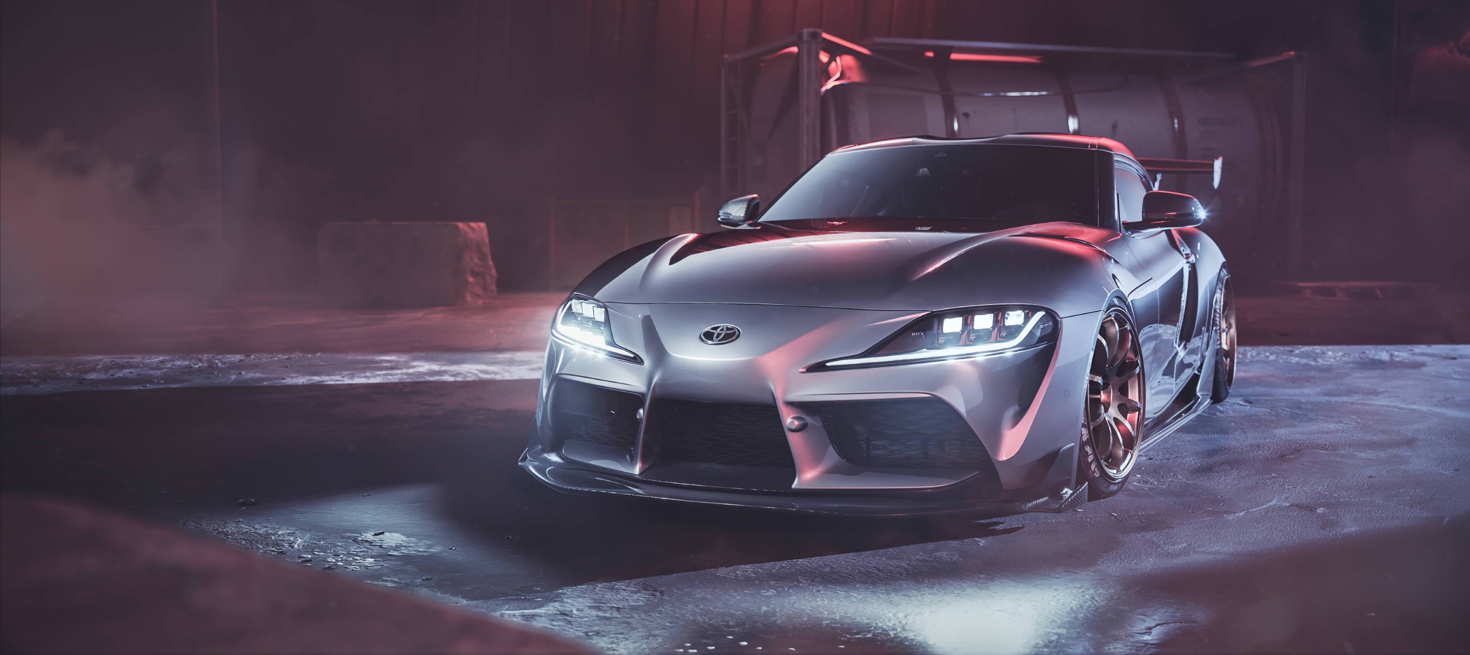 銀色 4K Supra 壁紙 — 一架時尚的銀色跑車在迷霧工業車庫中，於紅色環境燈光下散發著霓虹光芒。