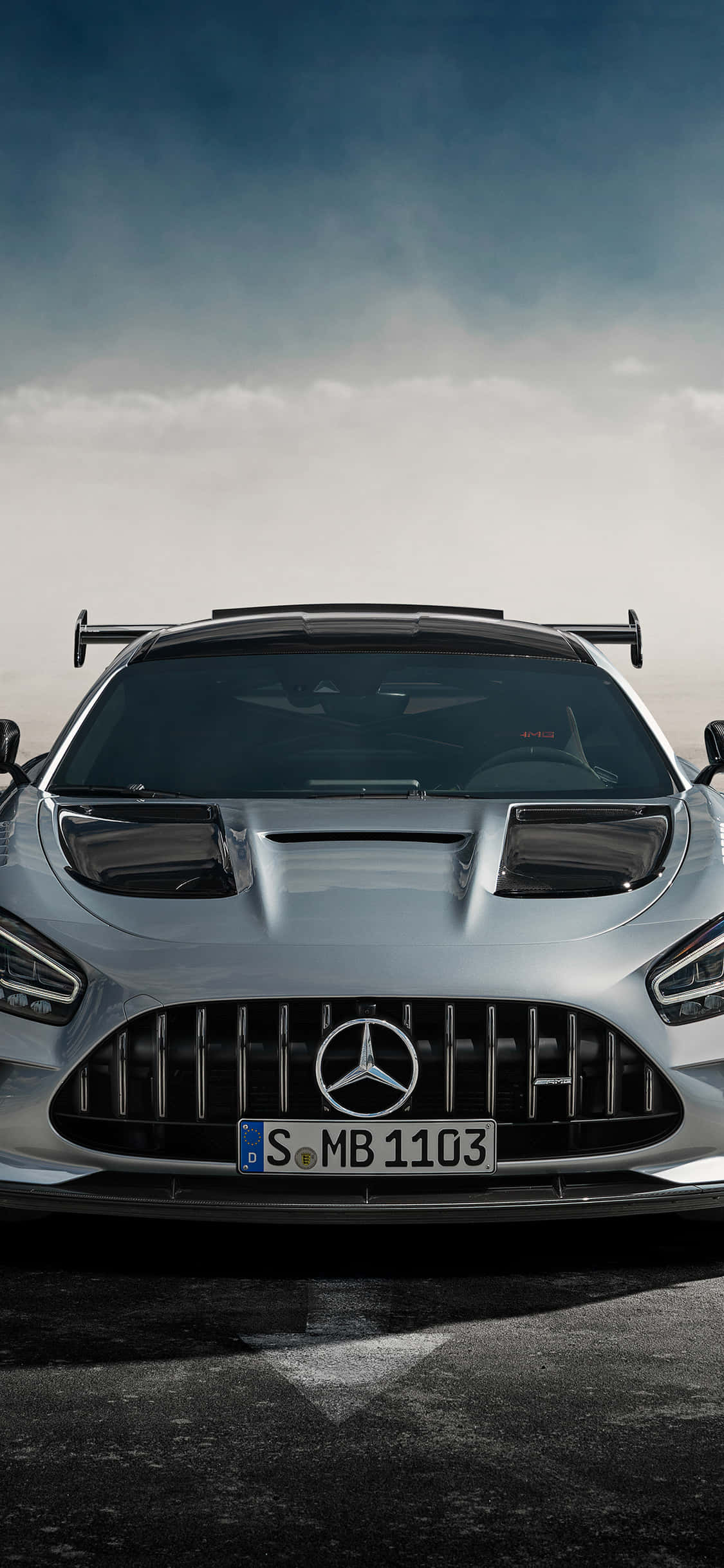 銀色 iPhone XS Mercedes AMG 藍天背景 壁紙 — 一架時尚的銀色 Mercedes-AMG GT R 跑車在戲劇性的多雲天空下，在潮濕的瀝青路上向前行駛。