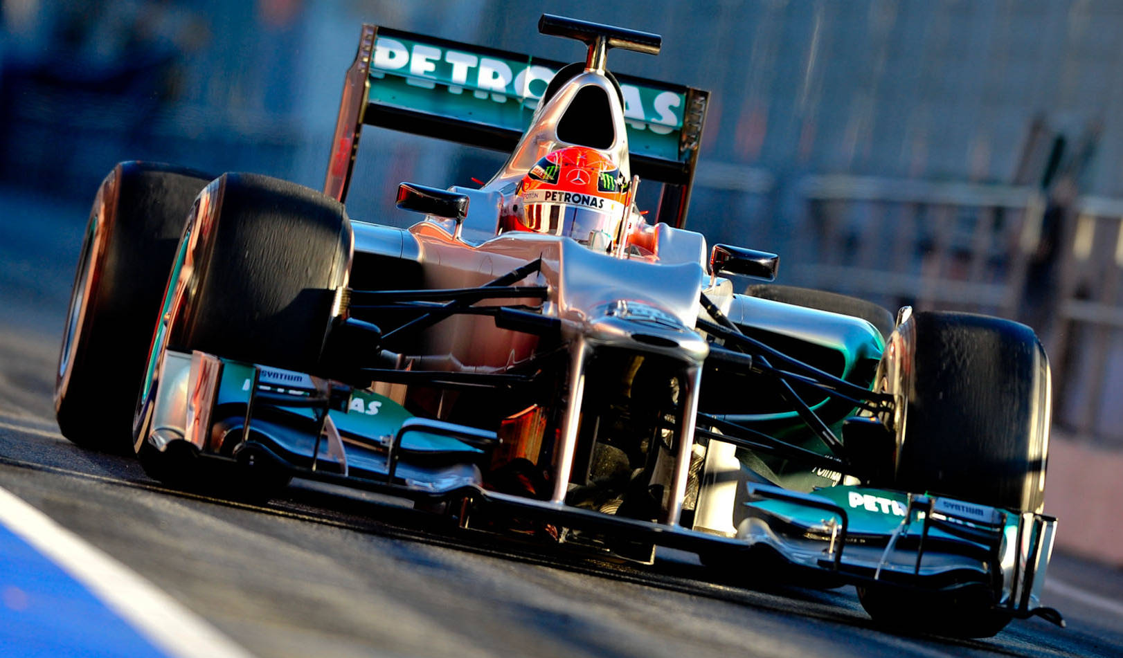 銀色 Petronas 邁克爾·舒馬赫 壁紙 — 一輛銀色和藍綠色的F1賽車帶有Petronas品牌標誌，在明亮的日光下沿著賽道飛馳。