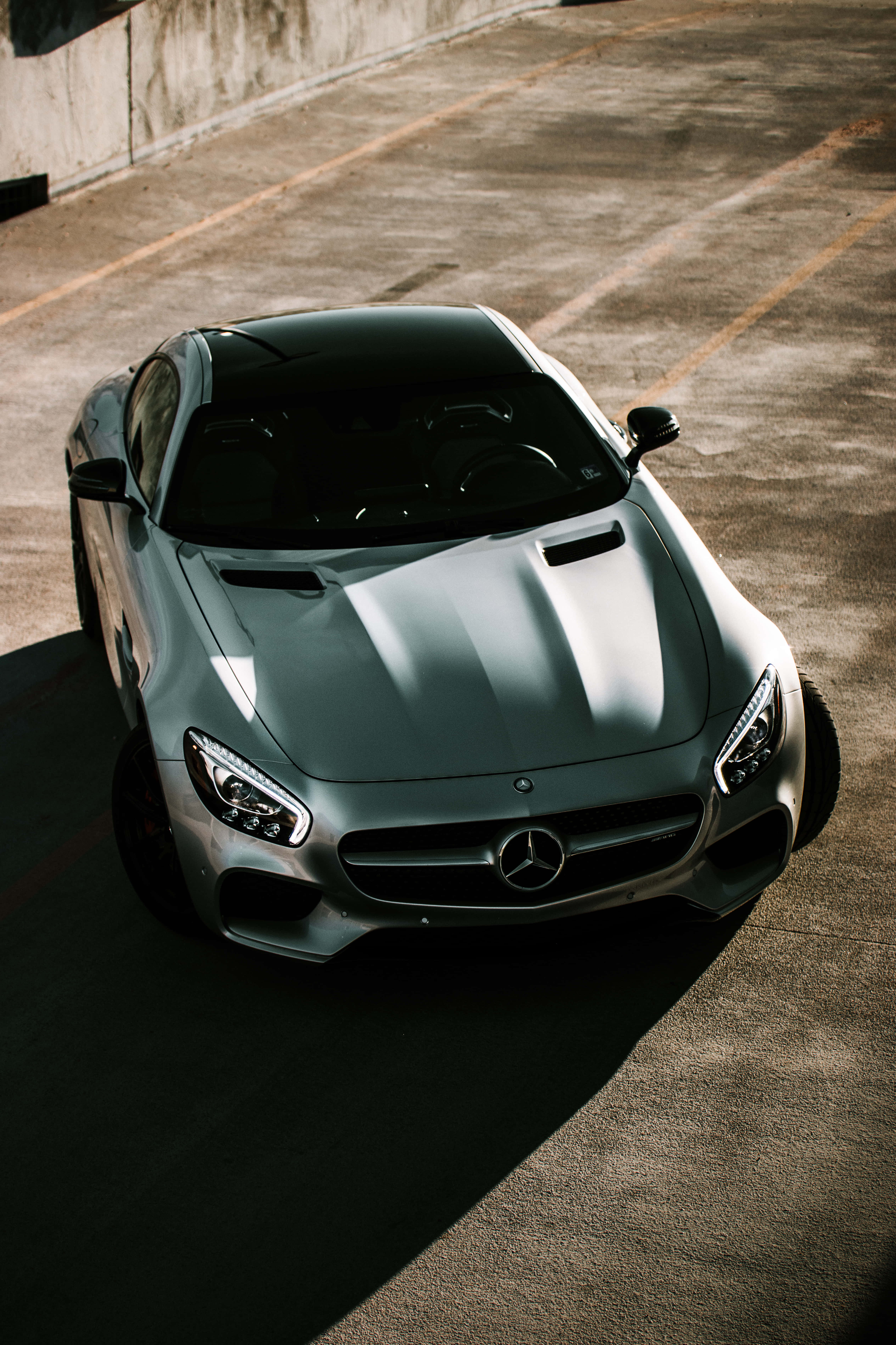 銀色AMG GT-R街景頂視圖壁紙 壁紙 — 一架時尚的銀色 Mercedes-AMG GT 停泊在陽光普照的混凝土停車場，投下長長的影子。