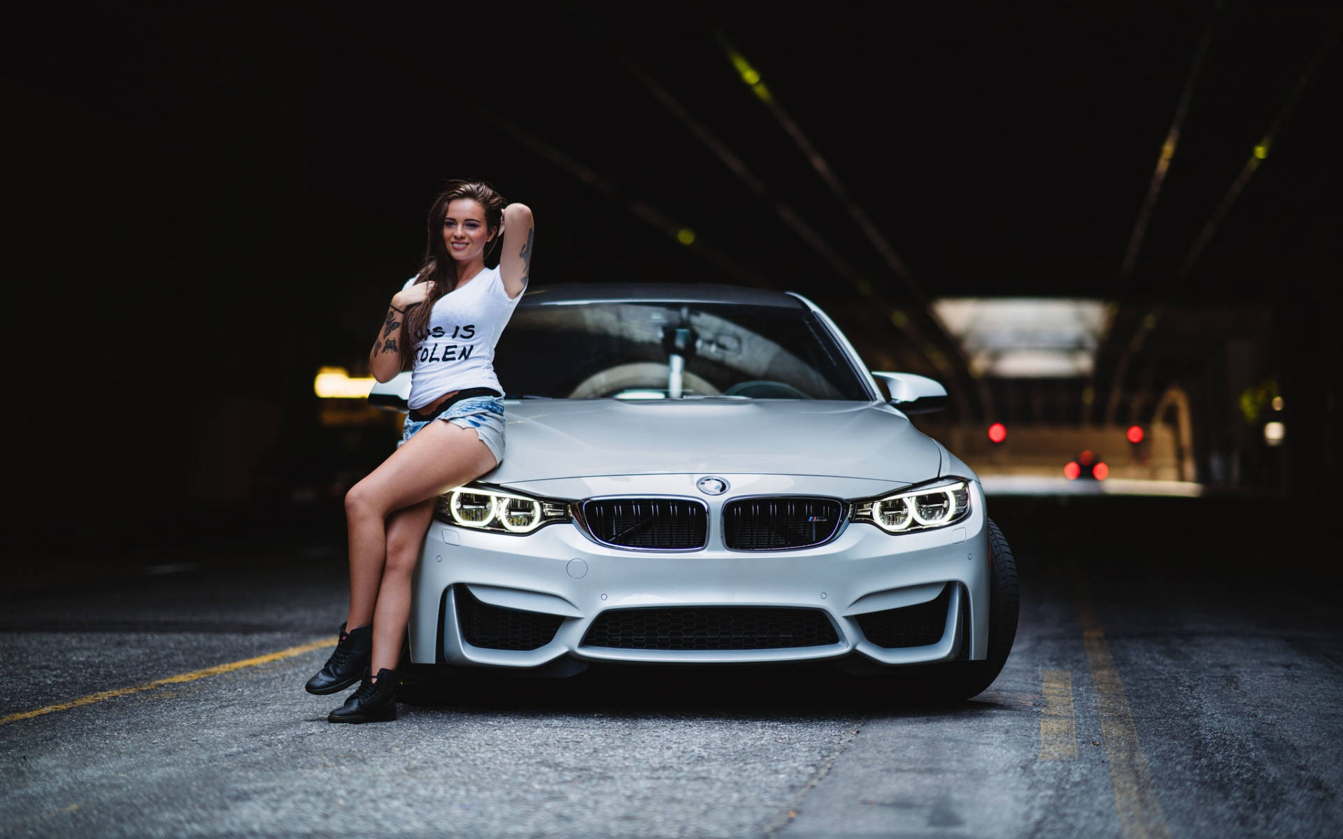 女性在夜晚的黑暗隧道中於銀色BMW M4引擎蓋上擺姿勢。