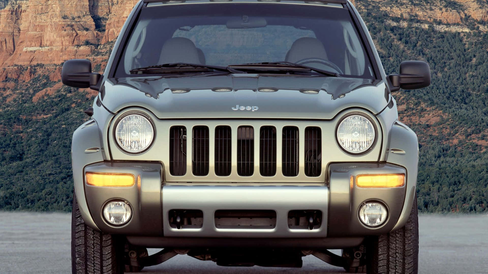 Jeep Liberty 桌布 壁紙 — 銀色Jeep Wrangler停喺紅色岩石懸崖同綠色森林前面嘅正面視圖。
