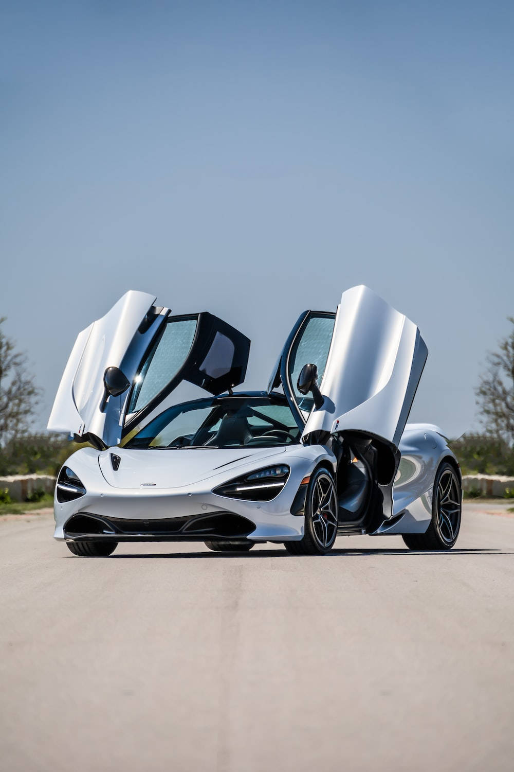 銀色McLaren 720S，鷗翼車門打開，停在鋪砌道路上。