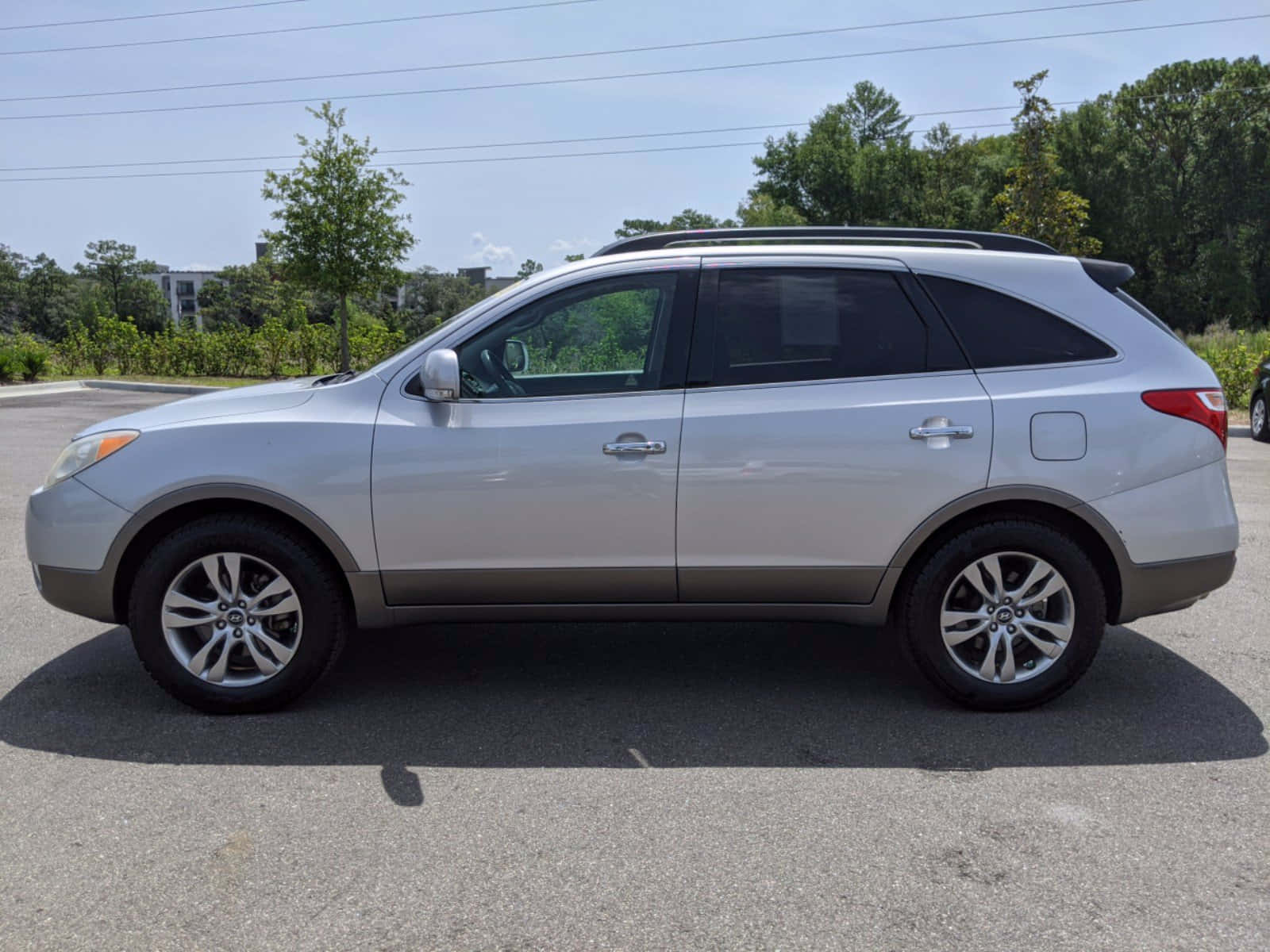 Hyundai Veracruz 桌布 壁紙 — 銀色SUV停泊在瀝青路上，背景有樹木和建築物，天空晴朗。