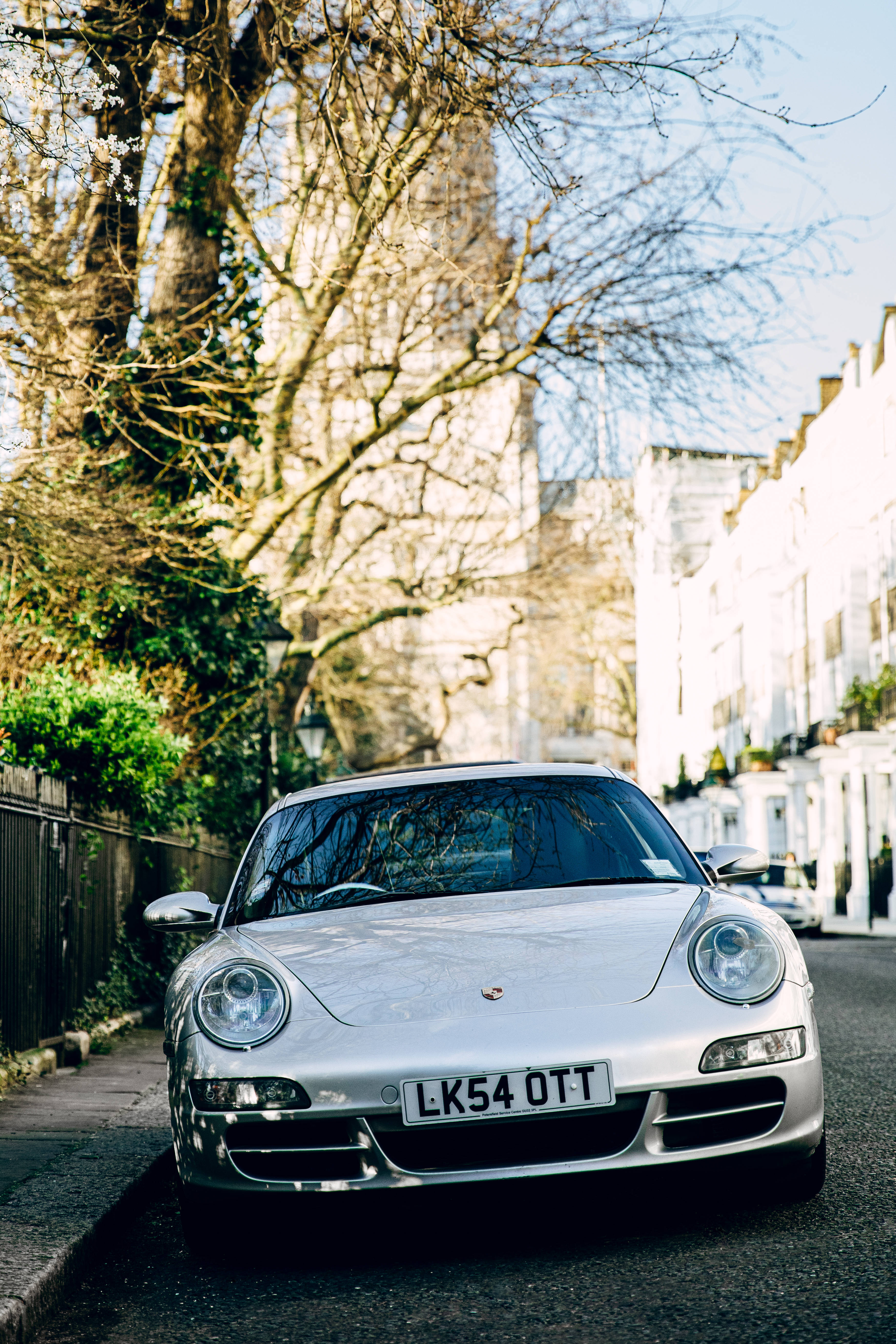 銀色保時捷911豪華跑車 壁紙 — 一輛銀色保時捷跑車停在陽光普照的住宅街道上，街道兩旁樹木成蔭。