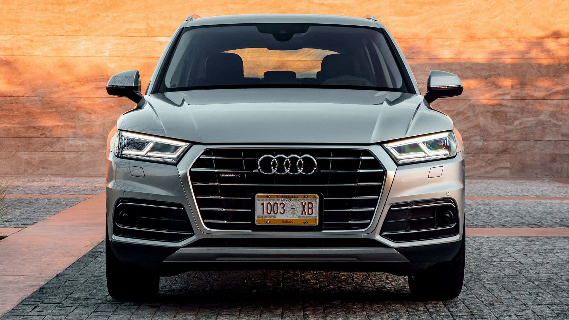 Audi Q5 桌布 壁紙 — 銀色奧迪Q5 SUV正面視圖，停泊在鵝卵石車道上，背景為暖色調磚牆。