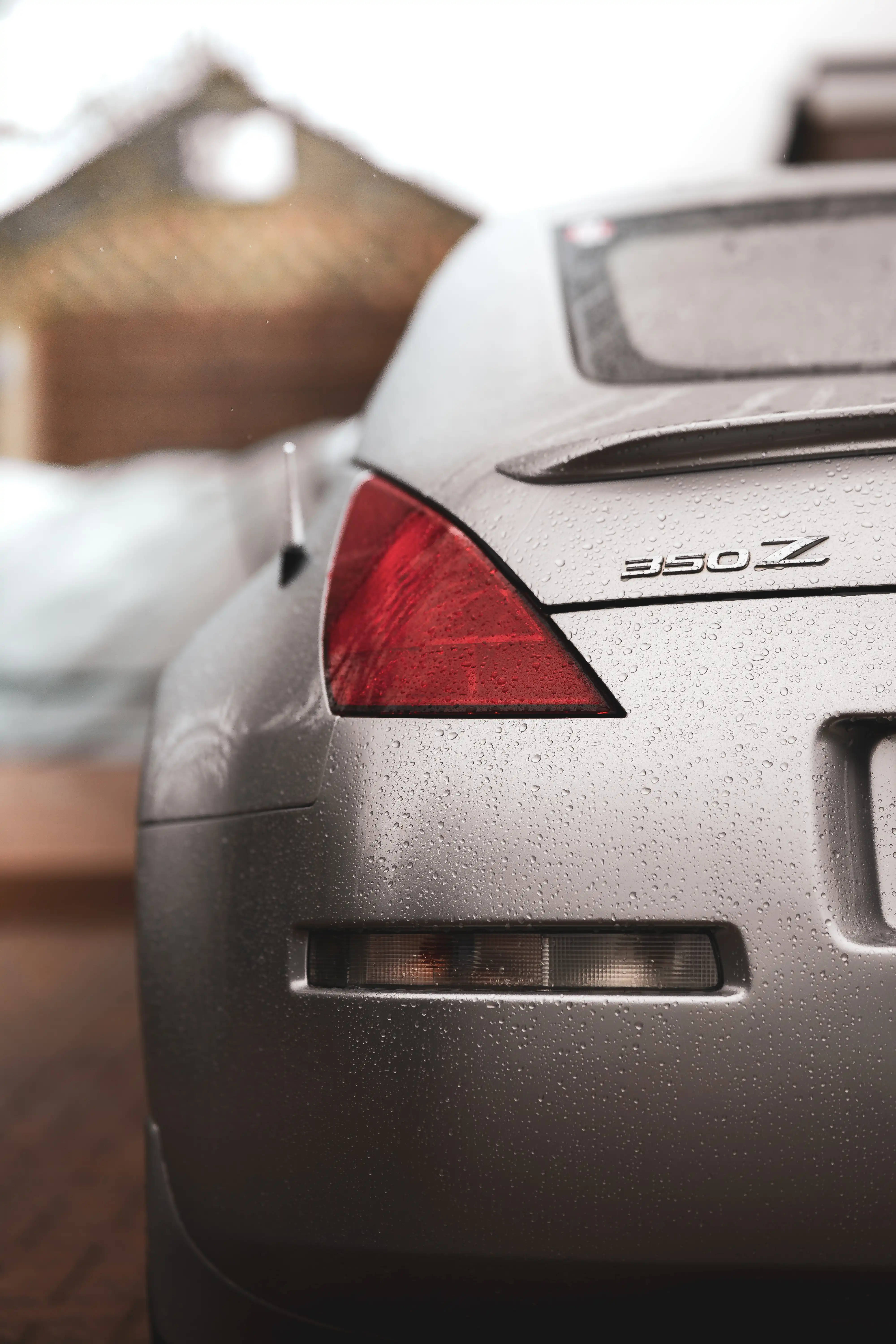Nissan 桌布 壁紙 — 銀色日產 Nissan 350Z 跑車尾部的特寫，表面上的雨滴在模糊的雪景背景下閃閃發光。