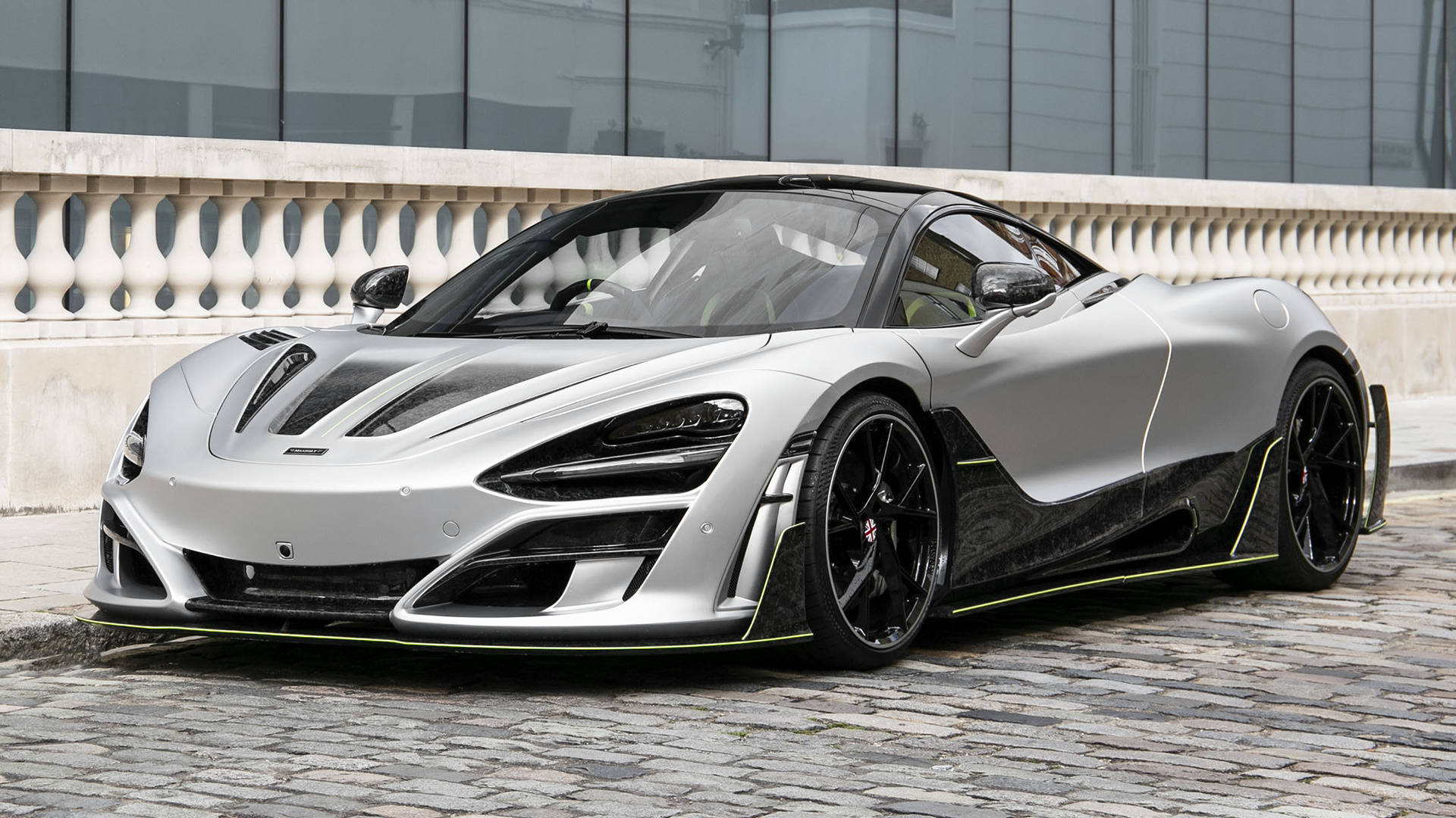 銀色曼索里麥拉倫720S 4K 壁紙 — 一輛時尚的銀色麥拿侖跑車，帶有黑色飾邊和螢光綠色裝飾，停在現代建築附近的鵝卵石街道上。