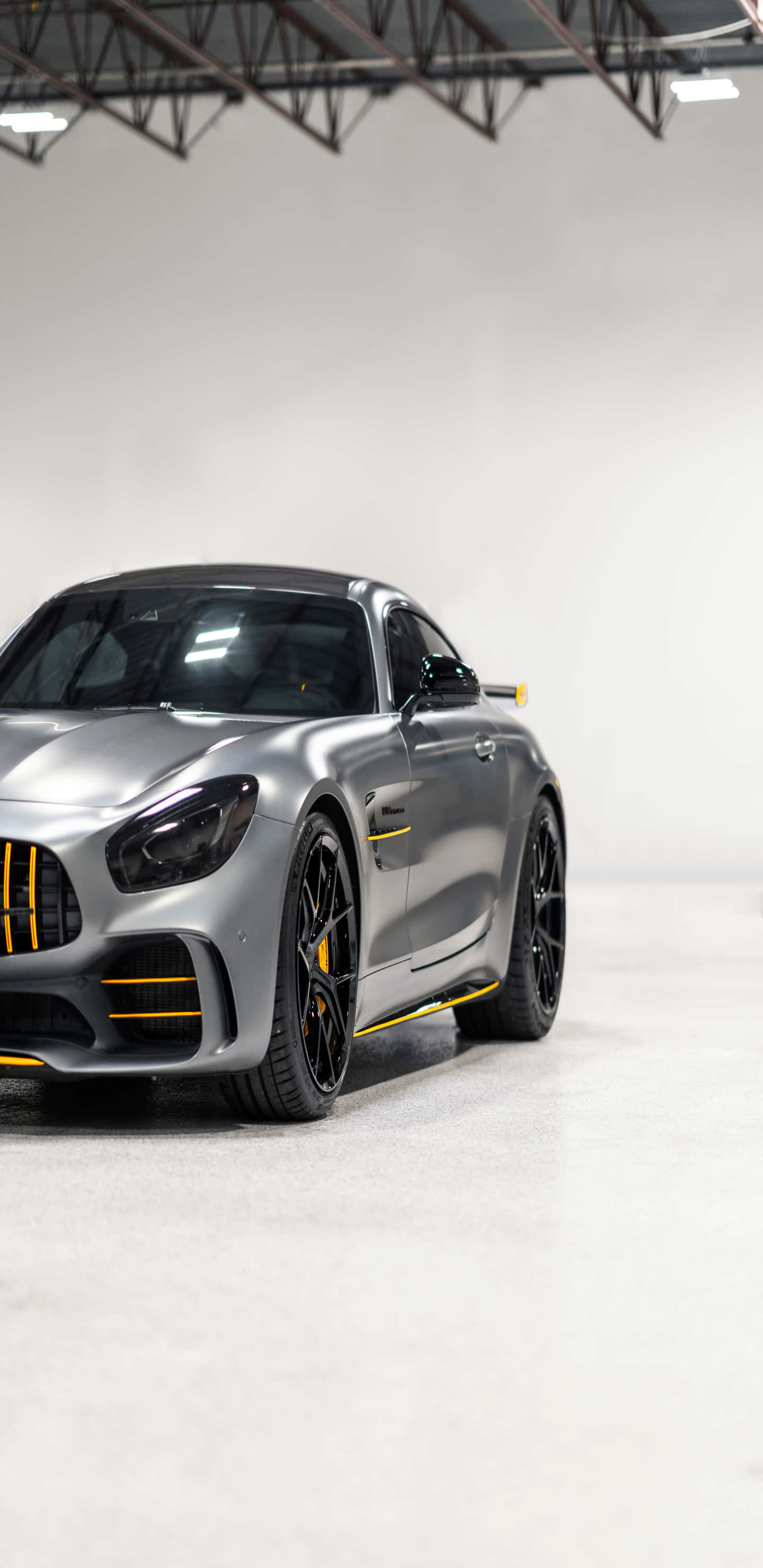 銀色梅賽德斯配黃色細節 Pixel 3XL AMG GT-R 背景 壁紙 — 一輛時尚的銀色 Mercedes-AMG GT R 跑車帶有黃色點綴，停在工業照明下的簡約白色車庫中。