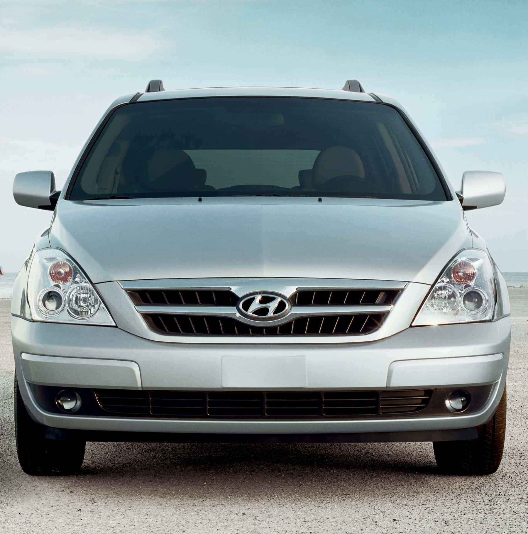 Hyundai Entourage 桌布 壁紙 — 銀色現代SUV停泊在礫石海灘上的正面視圖，背景有海洋和天空。