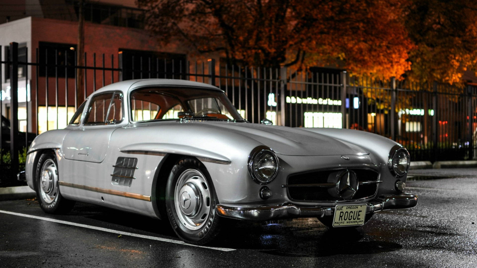 銀色 vintage Mercedes-Benz 300SL Gullwing 在夜間停泊在秋天的樹木下。