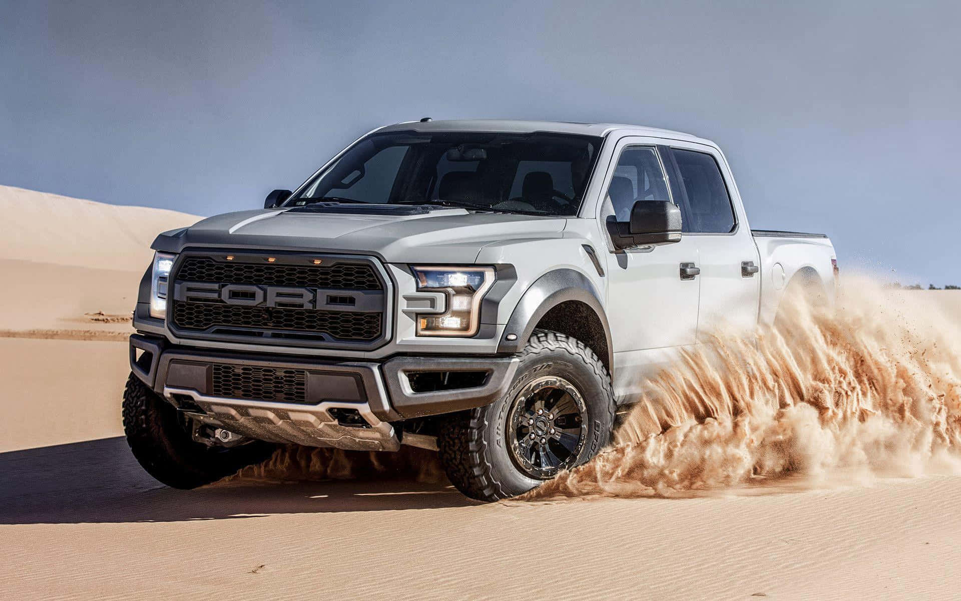 銀色福特 Raptor 貨車在黃昏時分駛過沙漠沙丘。