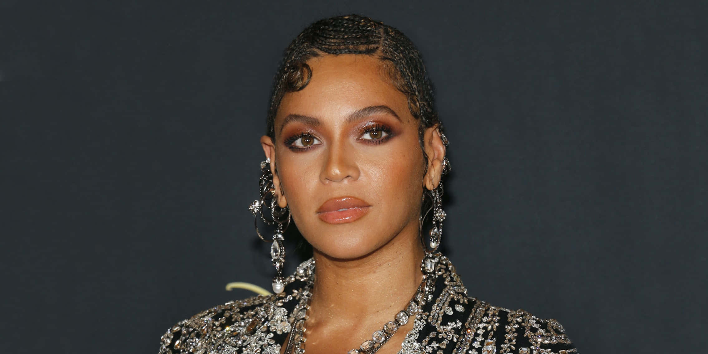 銀色閃耀——女王碧昂絲光芒四射 壁紙 — Beyoncé 在深色背景下，身穿閃亮黑色服裝，搭配精緻辮子髮型和垂墜耳環擺姿勢。