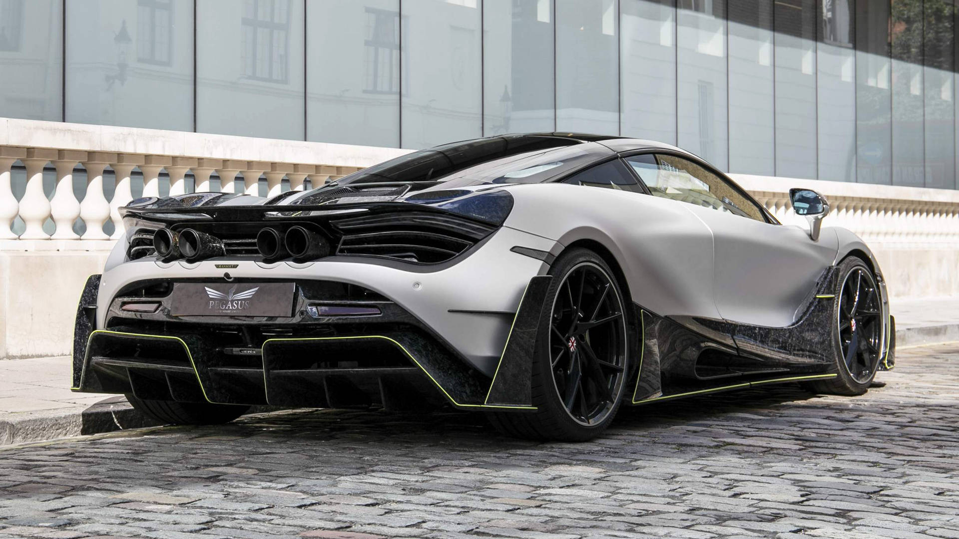 銀色麥拉倫720S 4K 壁紙 — 一輛啞光銀色McLaren 720S，帶有黑色飾邊和螢光黃色點綴，停泊在現代玻璃建築旁的鵝卵石街道上。