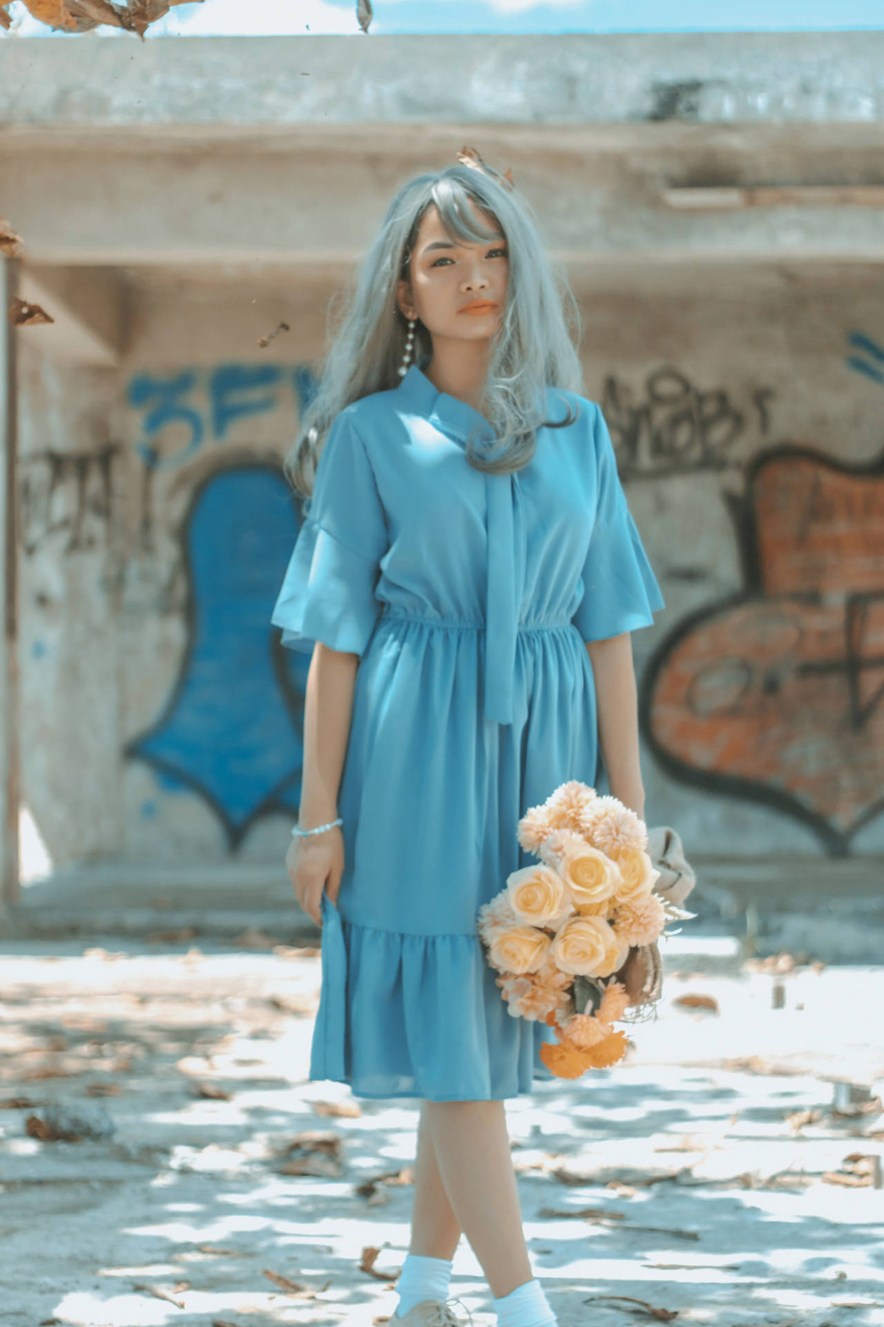 身穿藍色連衣裙的女子在塗鴉覆蓋的城市廢墟中手持蜜桃玫瑰。