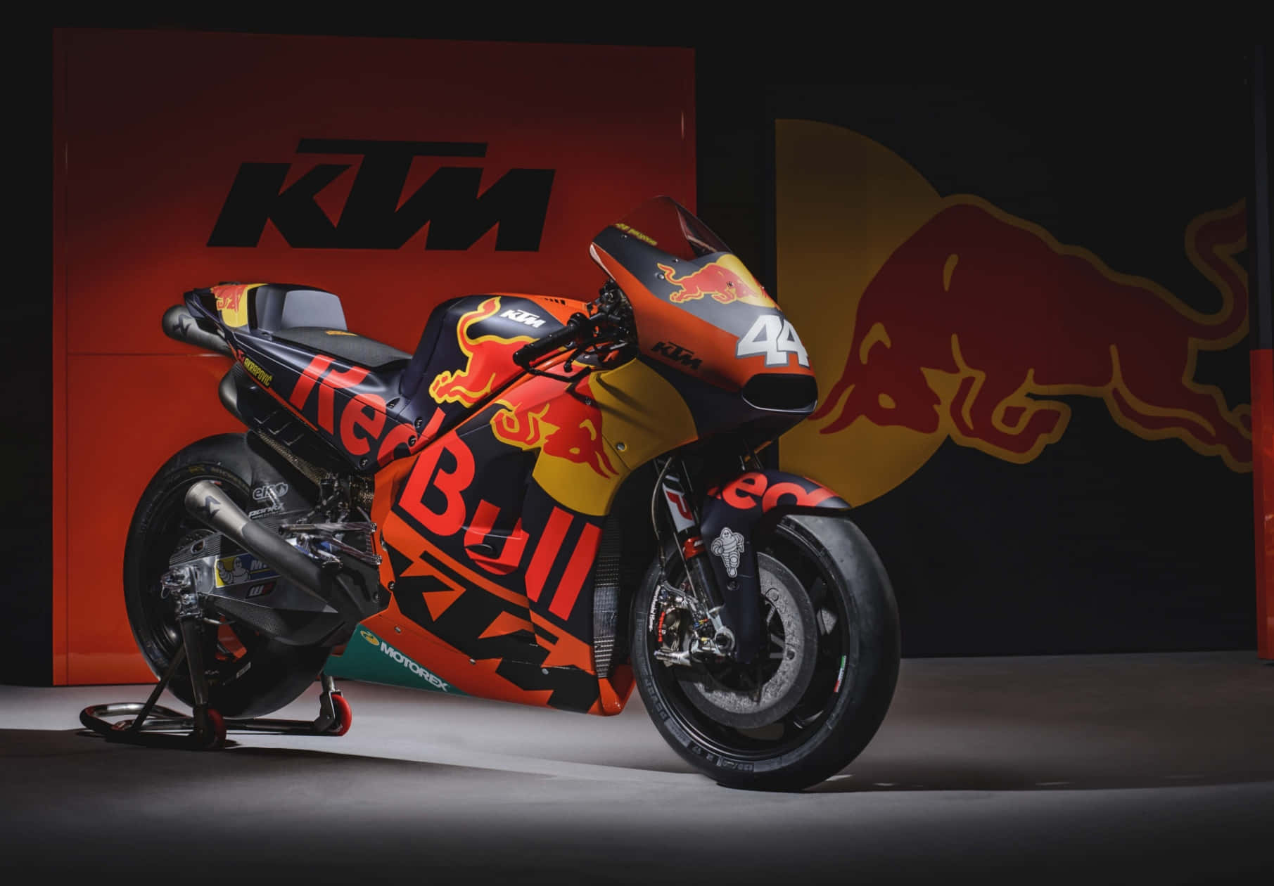 鋭利敏捷 - KTM摩托車動態展示 壁紙 — 一架型格嘅KTM MotoGP電單車配以Red Bull拉花，喺工作室場景中企喺品牌背景前面。