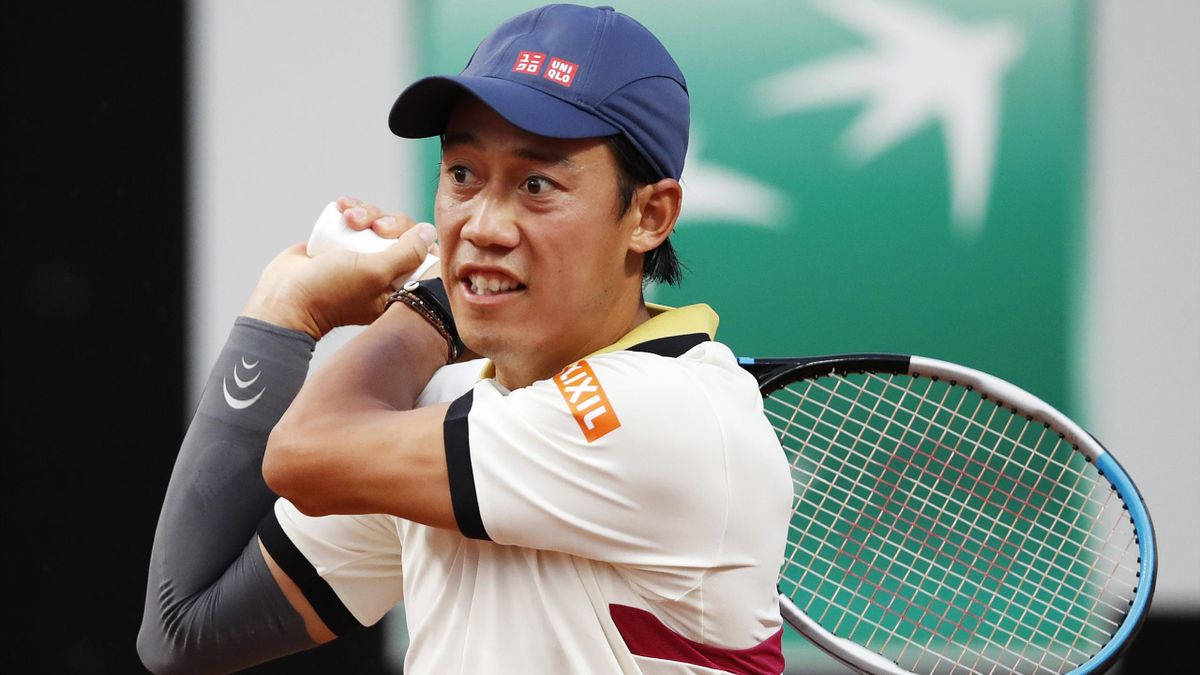 錦織圭揮舞Wilson球拍 壁紙 — 身穿藍色帽子和白色襯衫的網球選手在泥地球場比賽中專注地揮拍。