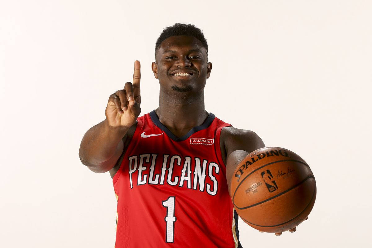 錫安·威廉森 數字一 壁紙 — 一位微笑的籃球運動員身穿紅色Pelicans球衣，手持Spalding籃球，在純白色背景上向上指。