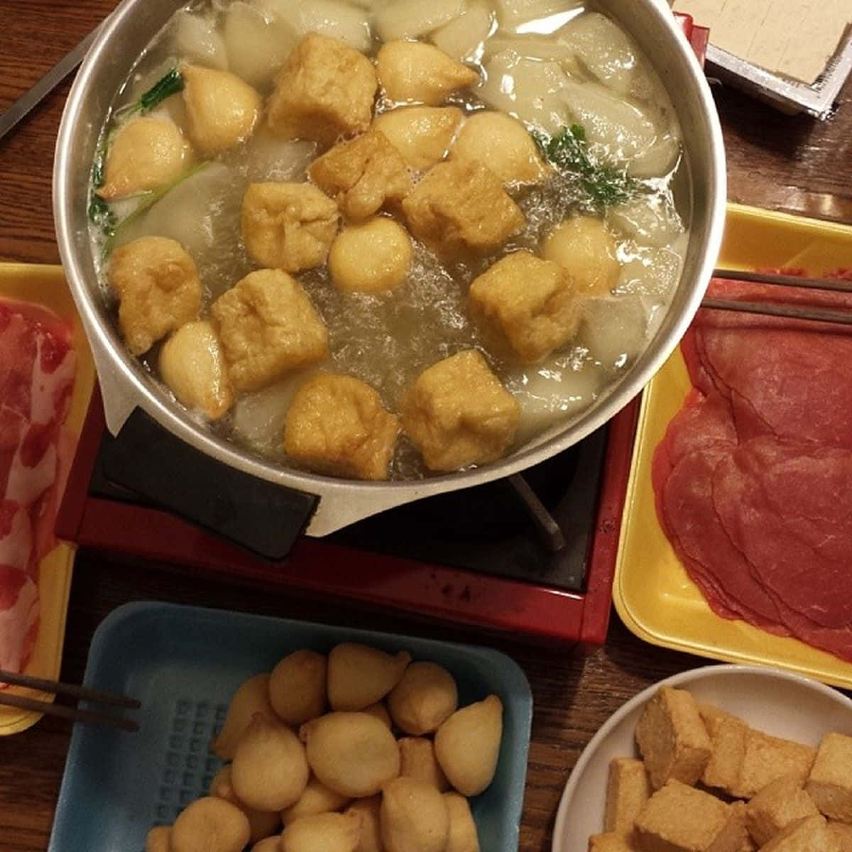 鍋中涮涮鍋料理 壁紙 — 一鍋冒煙的火鍋，裡面有豆腐魚丸和蔬菜，周圍放著生肉和餃子托盤。