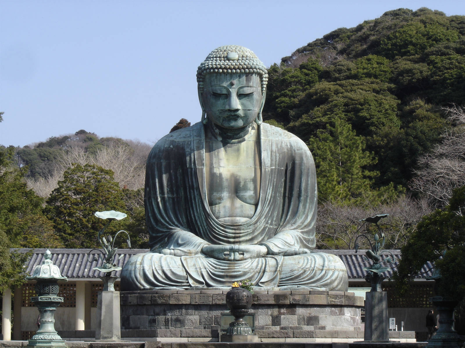 寺廟花園中的大型青銅佛像，背景有樹木和山脈。