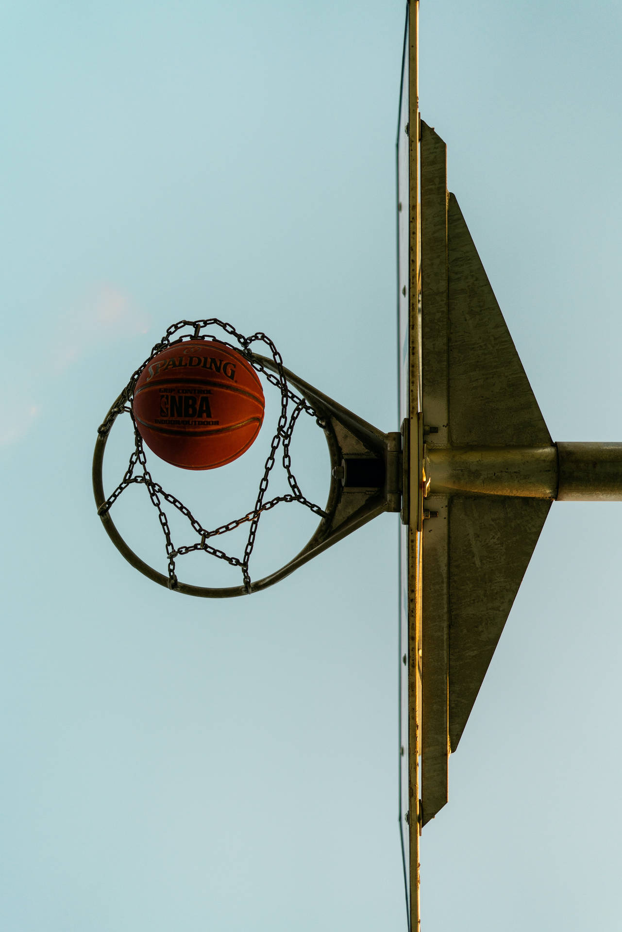 鏈條籃網底部視角 壁紙 — 一個 Spalding NBA 籃球完美地掛在鏈網籃框上，背景是清澈的淡藍色天空。