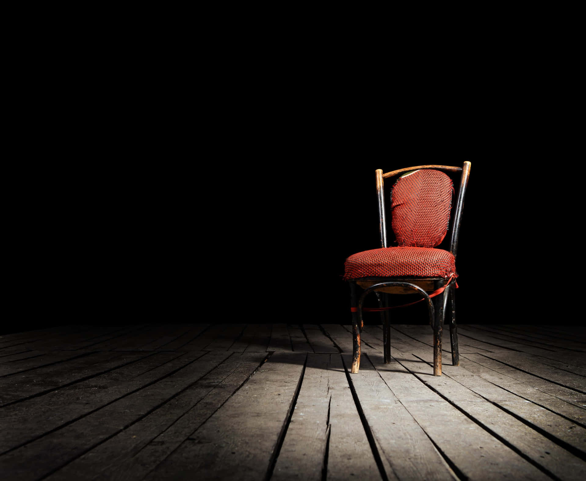 黑色背景的木地板上，聚光燈照亮的一張紅色椅子。