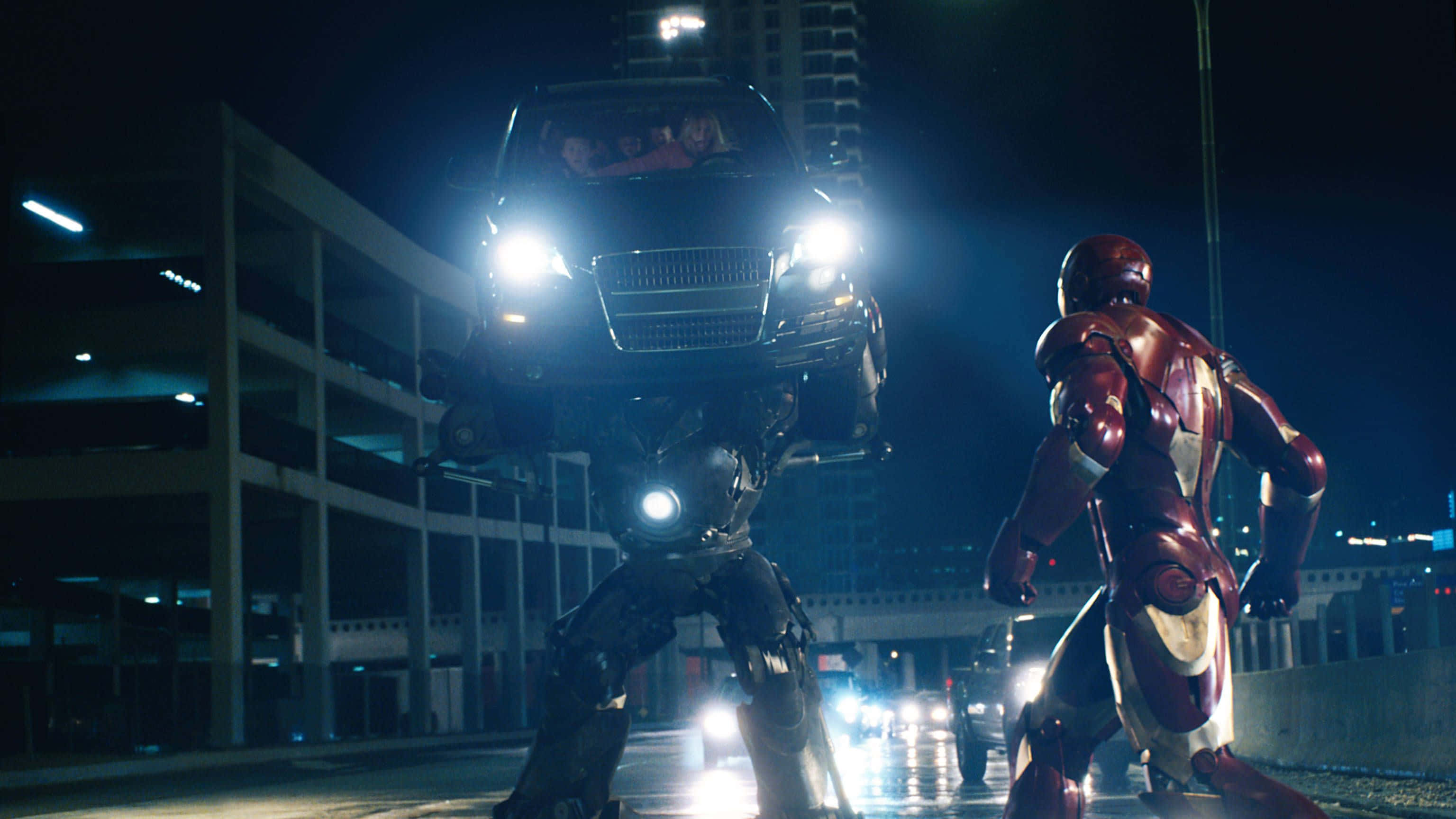 Iron Monger 桌布 壁紙 — 鐵甲奇俠在夜晚霓虹燈照亮的城市停車場中，面對一個拿著汽車的巨型機甲。