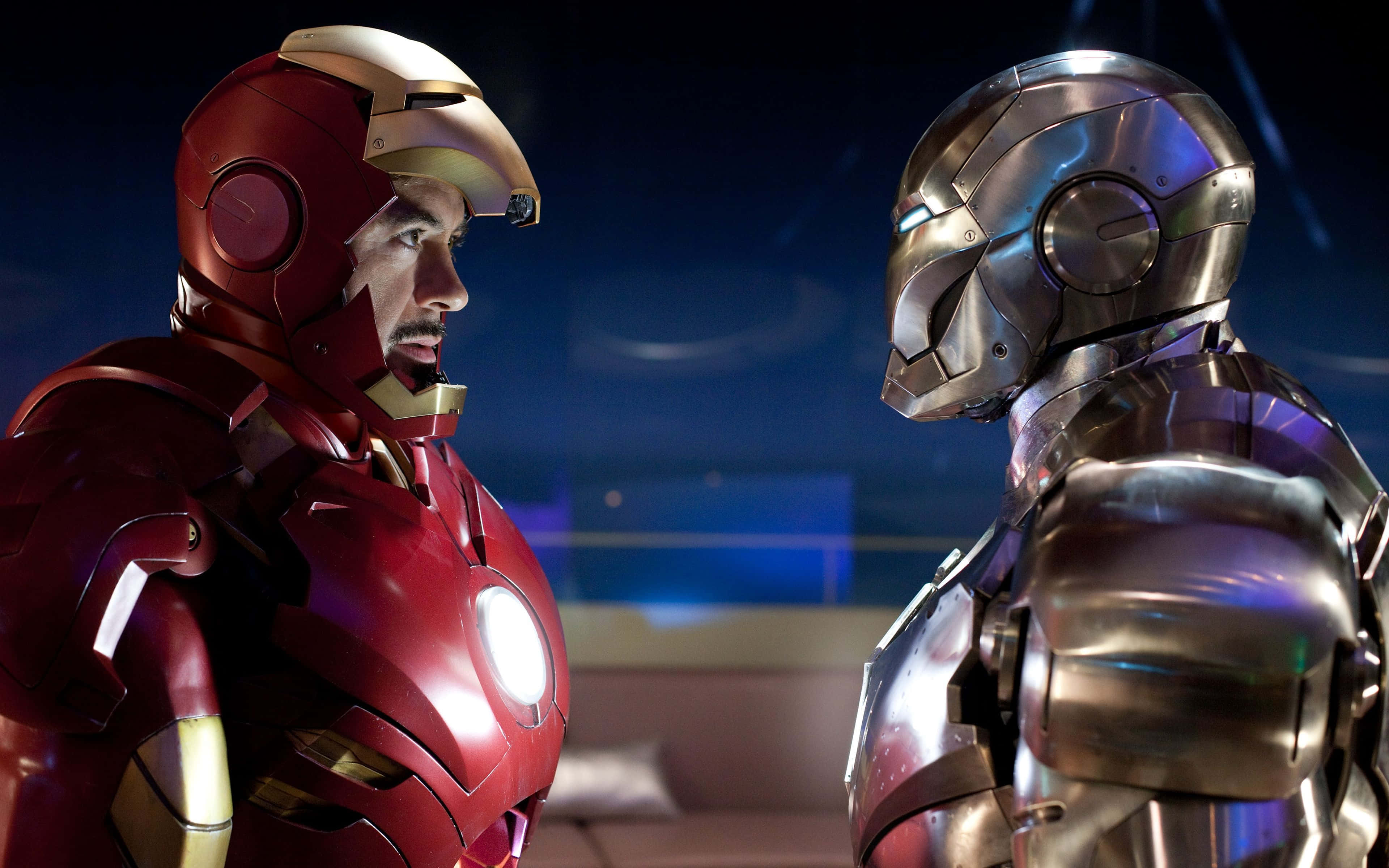 Iron Man Suit 桌布 壁紙 — 鐵甲奇俠與戰爭機器在昏暗的房間中對峙，裝甲發光，表情激烈。