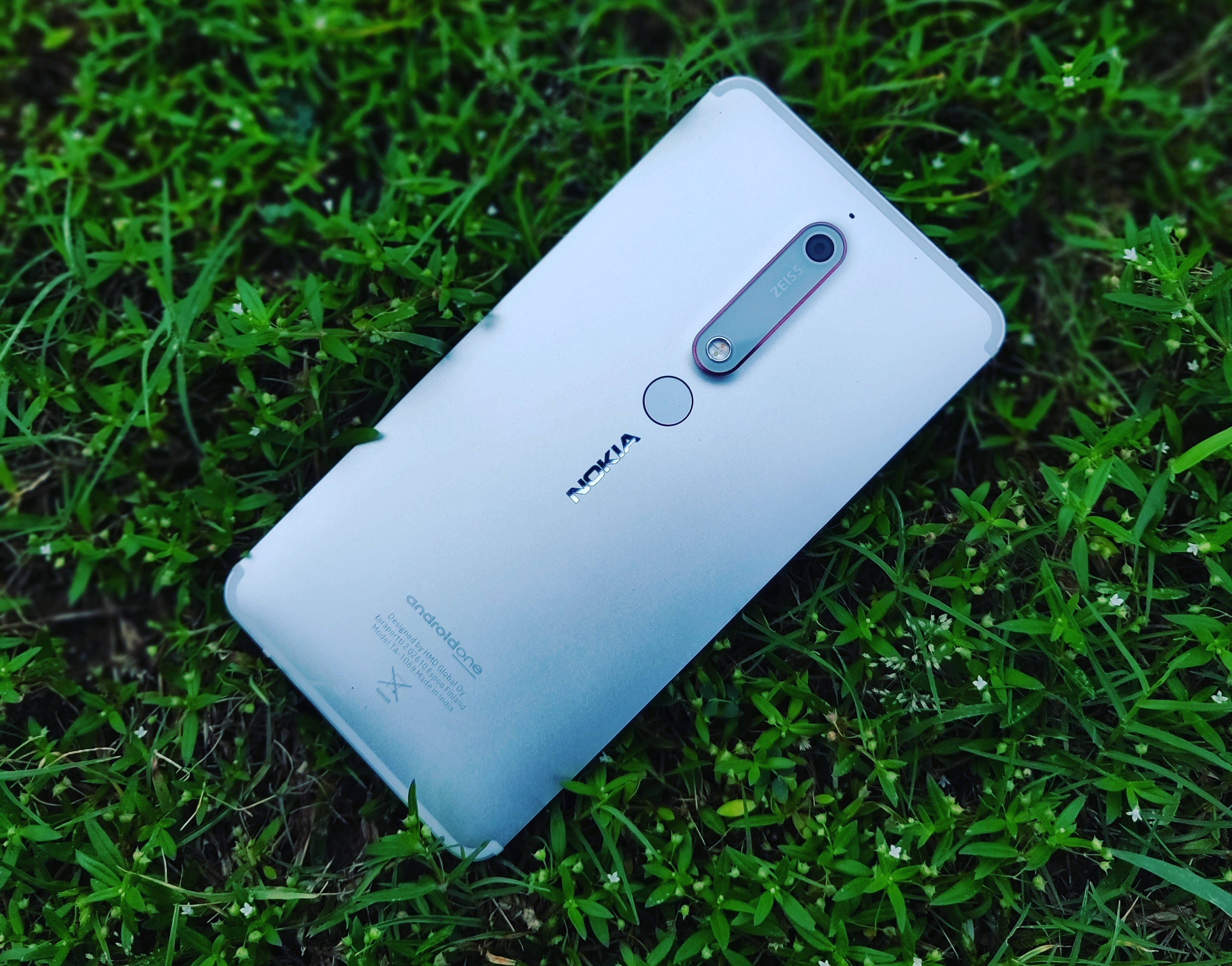 鐵藍色諾基亞 6.1 後蓋 壁紙 — 一部銀色 Nokia 智能手機對角放置在點綴著細小白花的鮮綠色草地上。