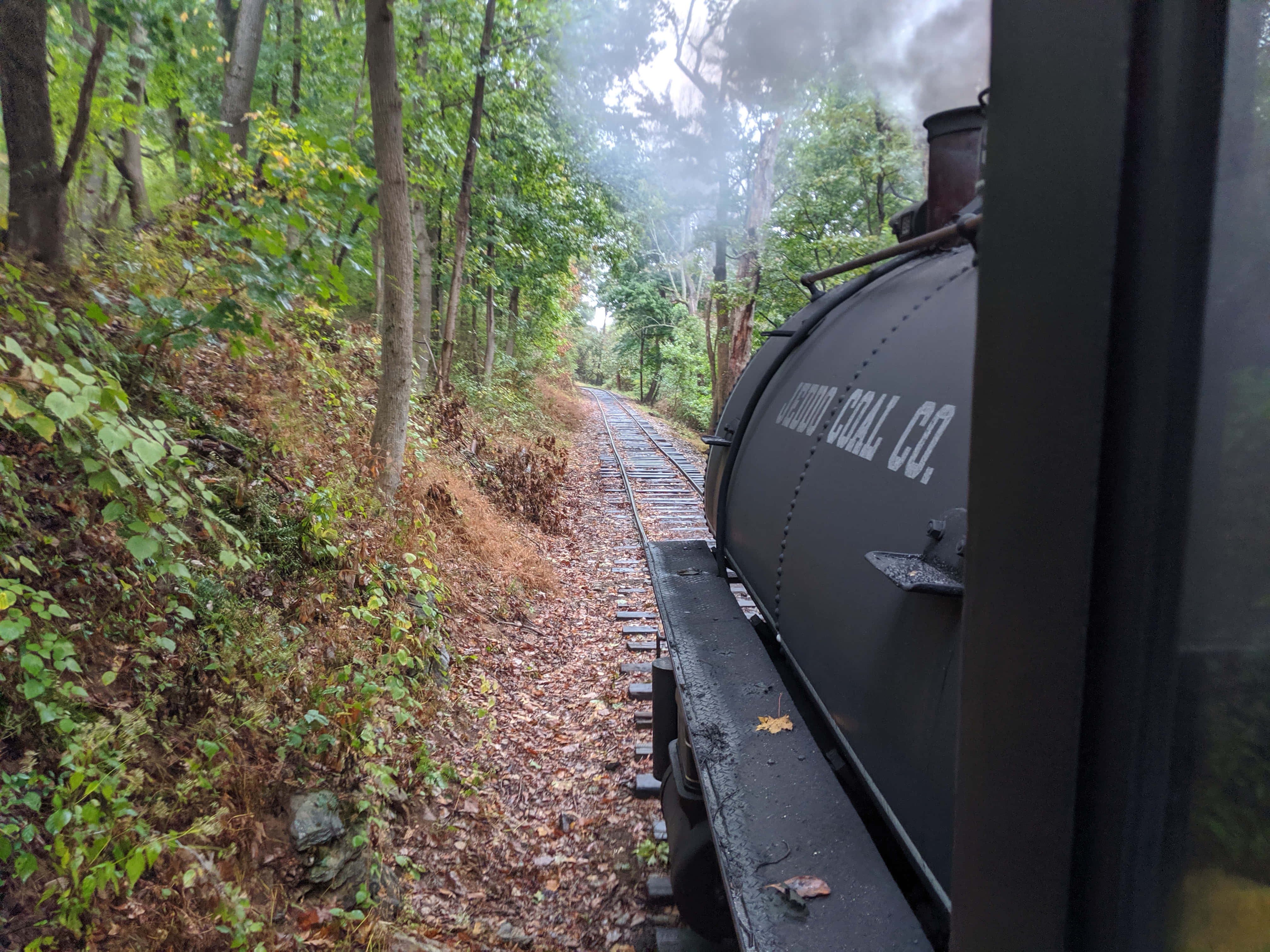 鐵路軌道上的壯麗日落 壁紙 — 一輛側面寫有「HUNTINGTON COAL CO.」的復古蒸汽火車，穿過落葉滿地、樹木迷霧的茂密森林。