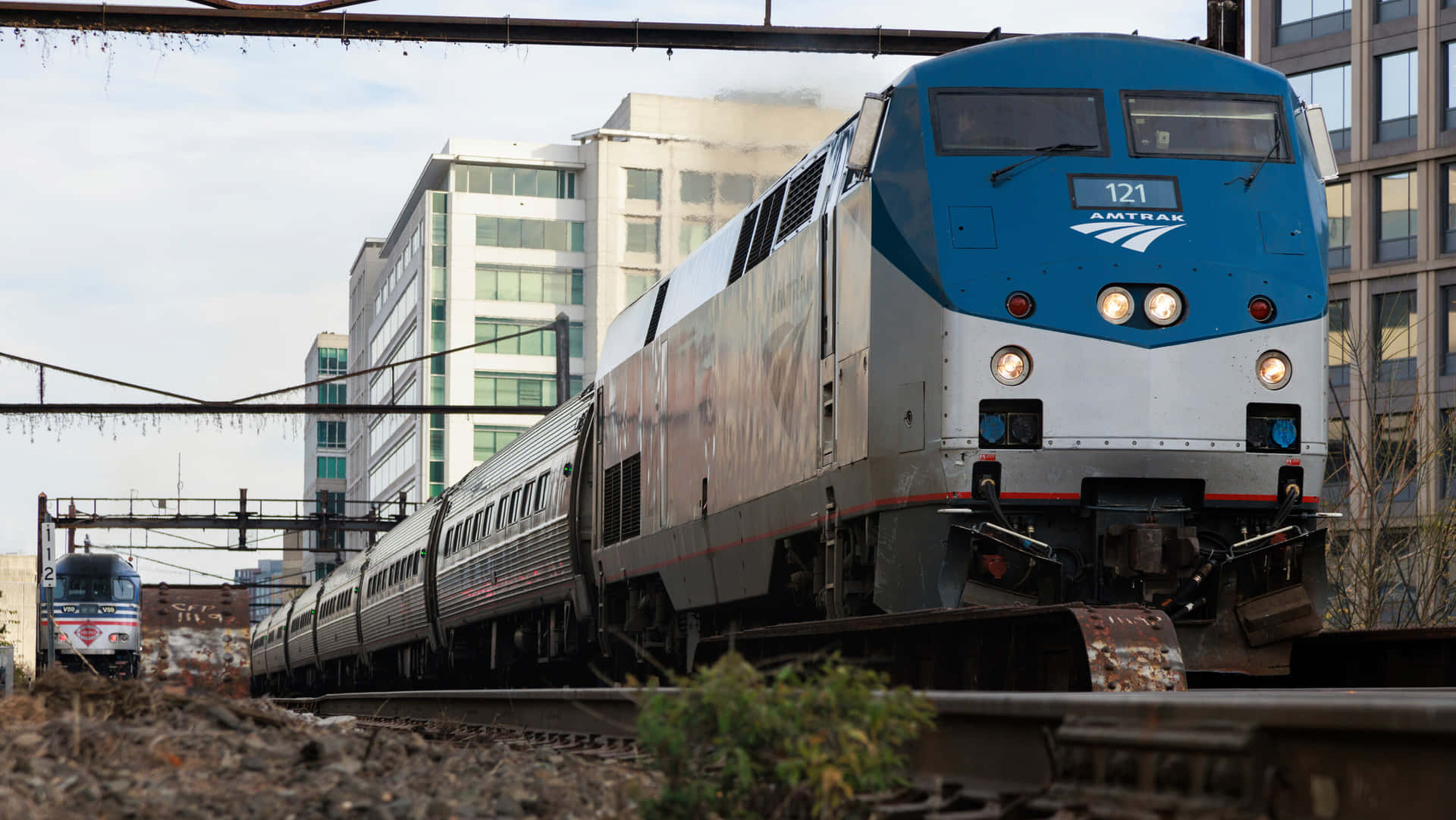 Amtrak火車在城市鐵路調車場中行駛，後面是高樓大廈。