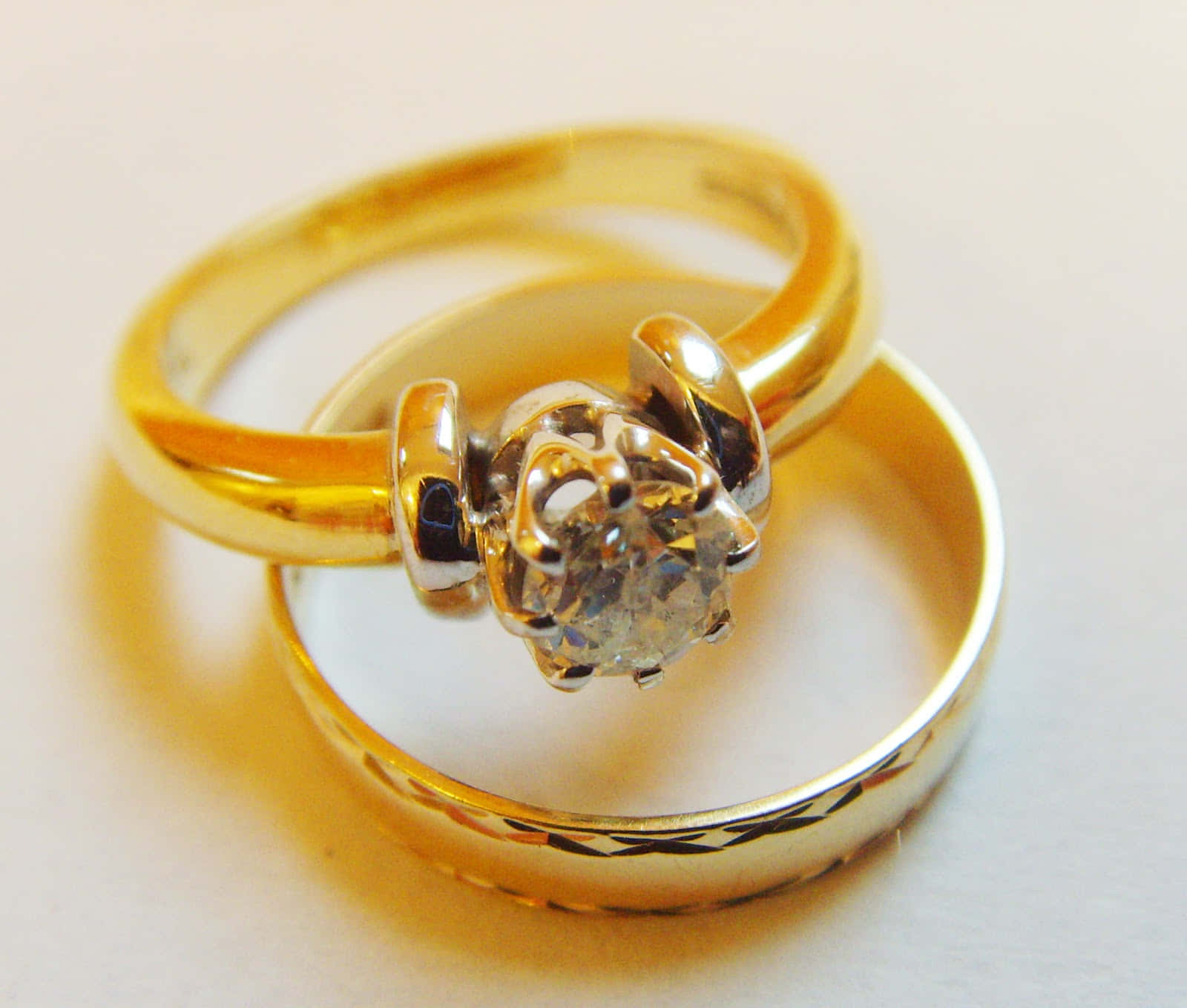 兩枚金結婚戒指，一枚鑲有單鑽，交纏在白色表面上