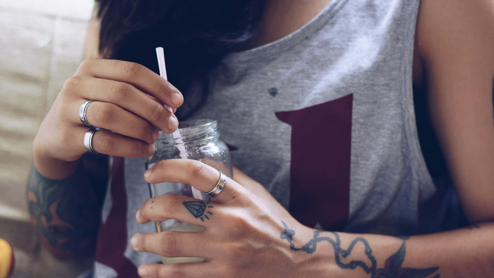 鑽石與念珠手部紋身 壁紙 — 近距離拍攝一位有紋身的人手持帶有吸管的玻璃罐。