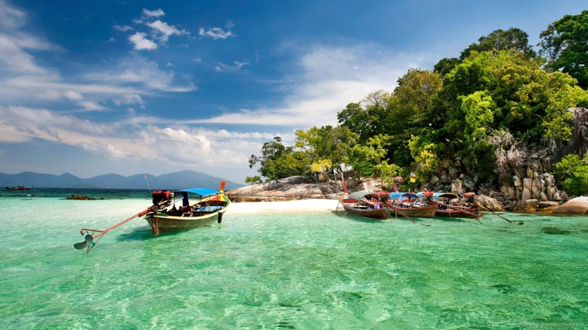 Thailand Beach 桌布 壁紙 — 長尾船停泊在 pristine 白色沙灘上，四周環繞著碧綠的海水和茂密的綠色叢林，頭頂是明亮的藍天。